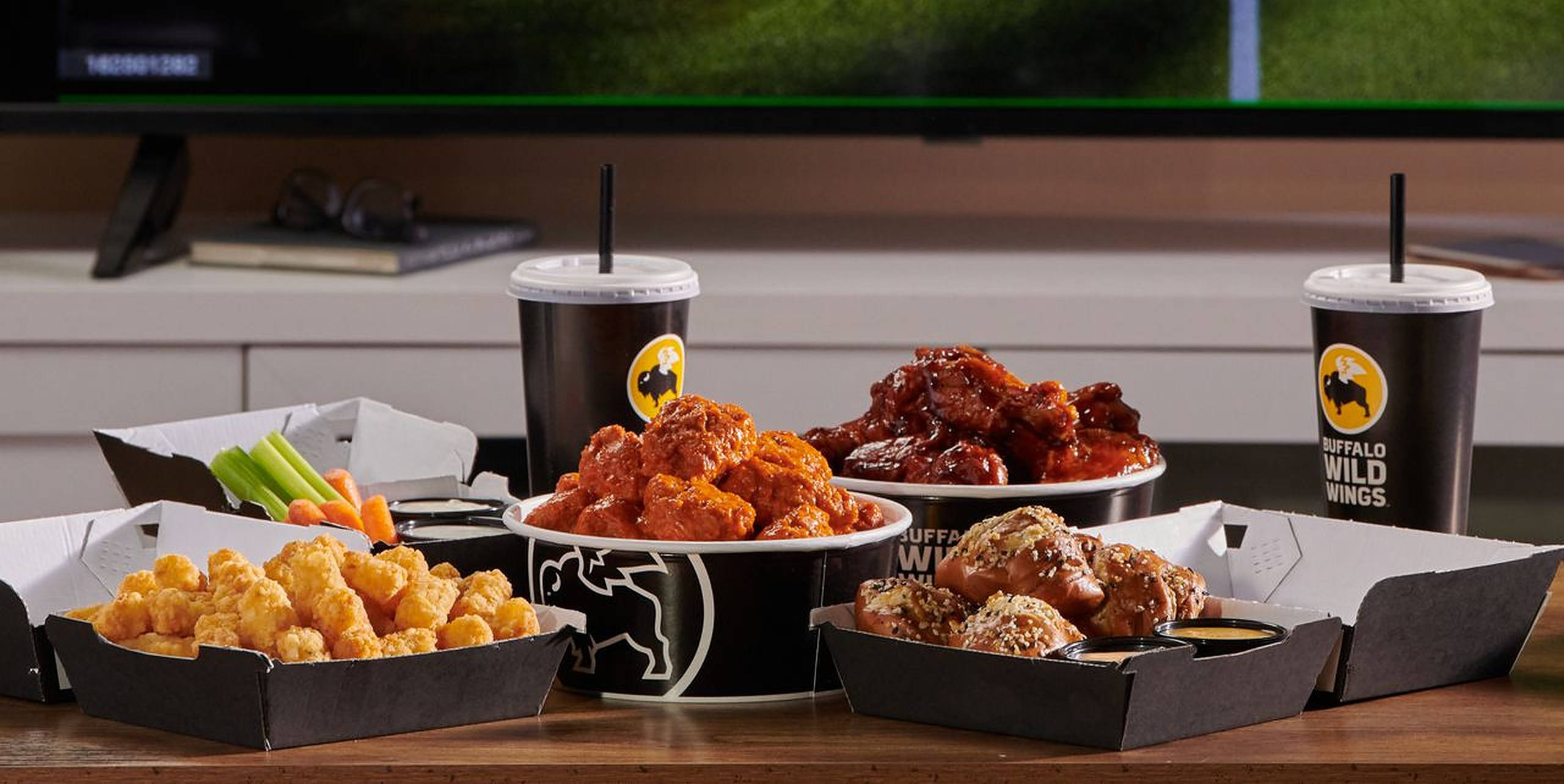 Buffalo Wild Wings 足球菜單 壁紙 — Buffalo Wild Wings 美食的誘人拼盤，包括雞翼、薯球和芹菜條，擺放在木桌上。