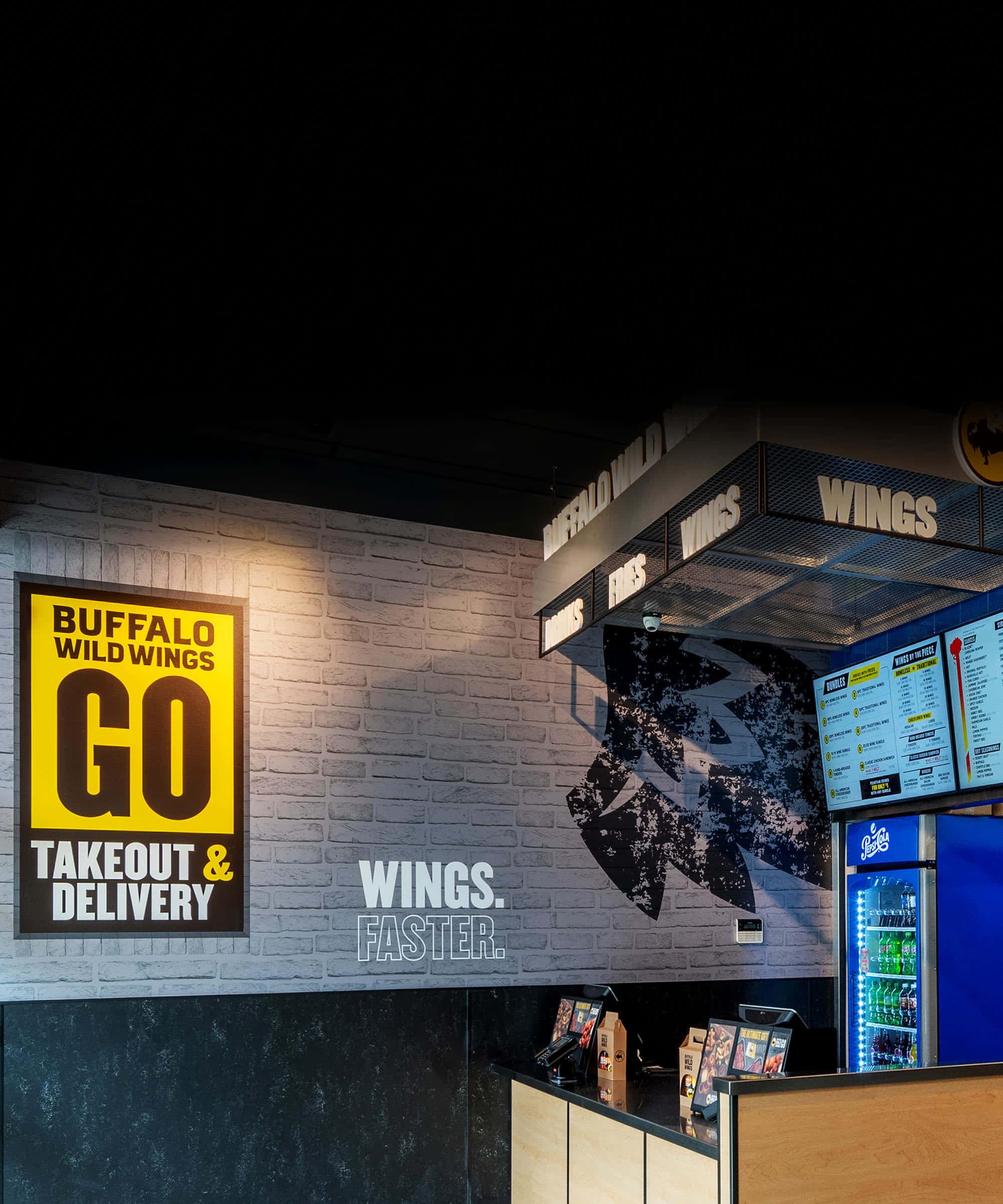 Buffalo Wild Wings招牌燈箱在夜空下閃耀 壁紙 — 燈光昏暗的Buffalo Wild Wings餐廳內部，磚牆被霓虹燈招牌和發光的飲料冷卻器照亮。