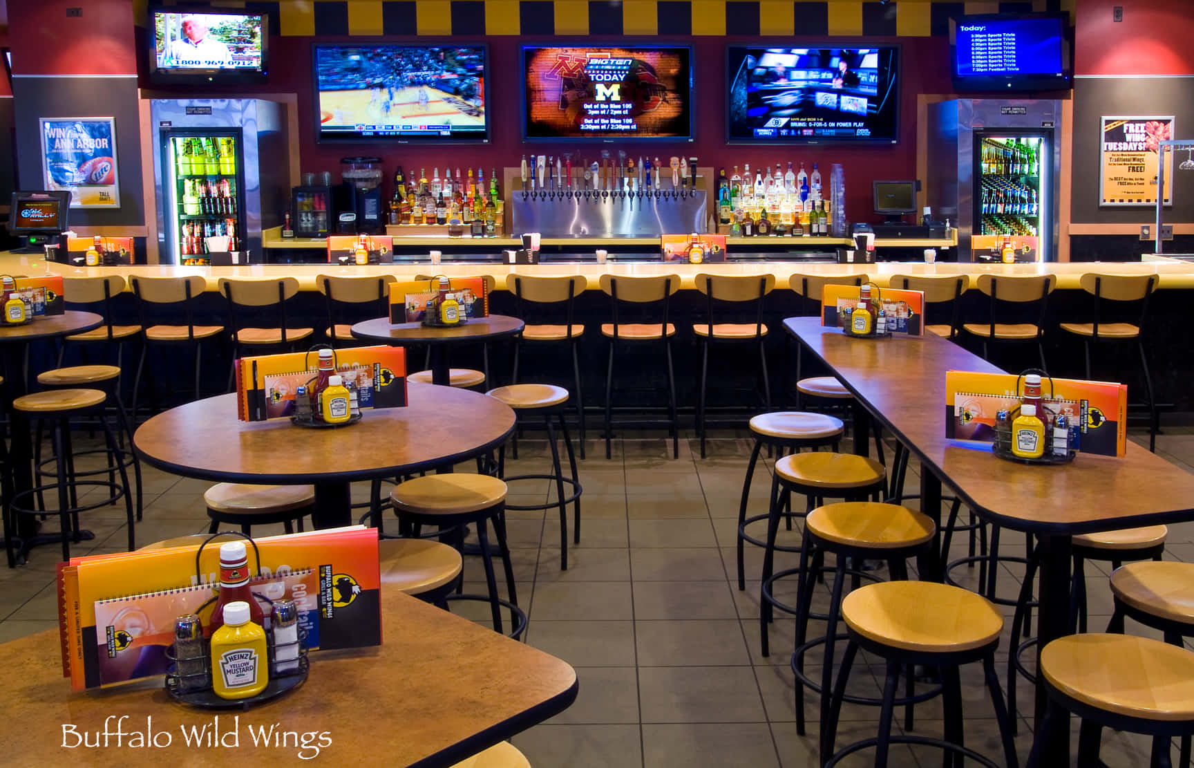 體驗Buffalo Wild Wings的正宗風味 壁紙 — 燈光明亮的Buffalo Wild Wings餐廳，設有木製桌椅，多部電視播放體育賽事，吧枱存貨充足。