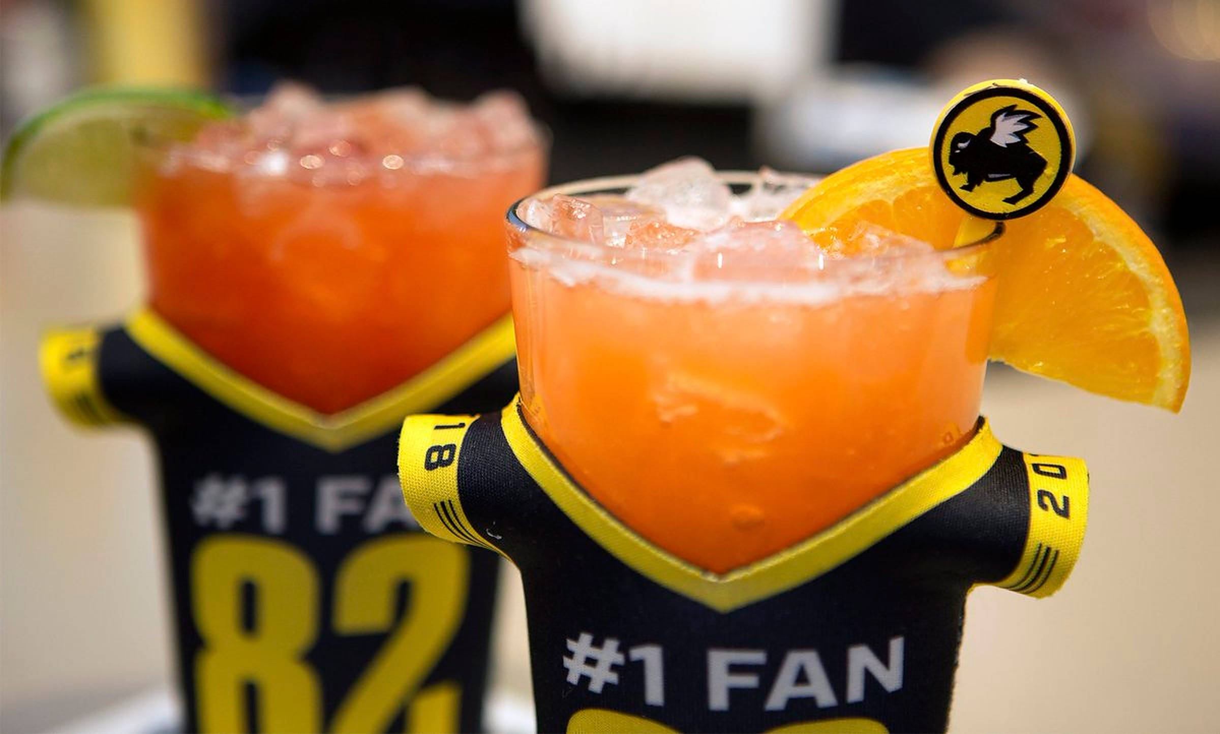 Buffalo Wild Wings 飲品 壁紙 — 兩杯充滿活力的橙色雞尾酒，置於黑色和黃色運動球衣架中，飾以橙片和青檸角。