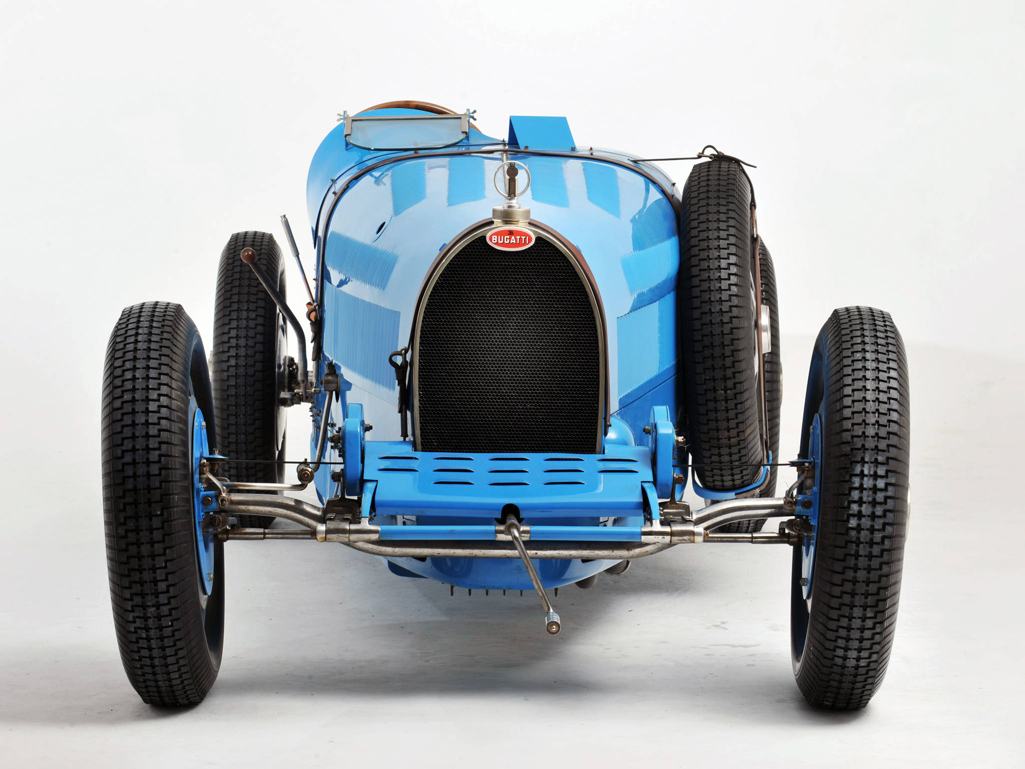 藍色 Bugatti Type 35 前視 iPhone 壁紙 — 一輛復古藍色Bugatti賽車，帶有外露底盤和備用輪胎，在純白色工作室背景前蓄勢待發。