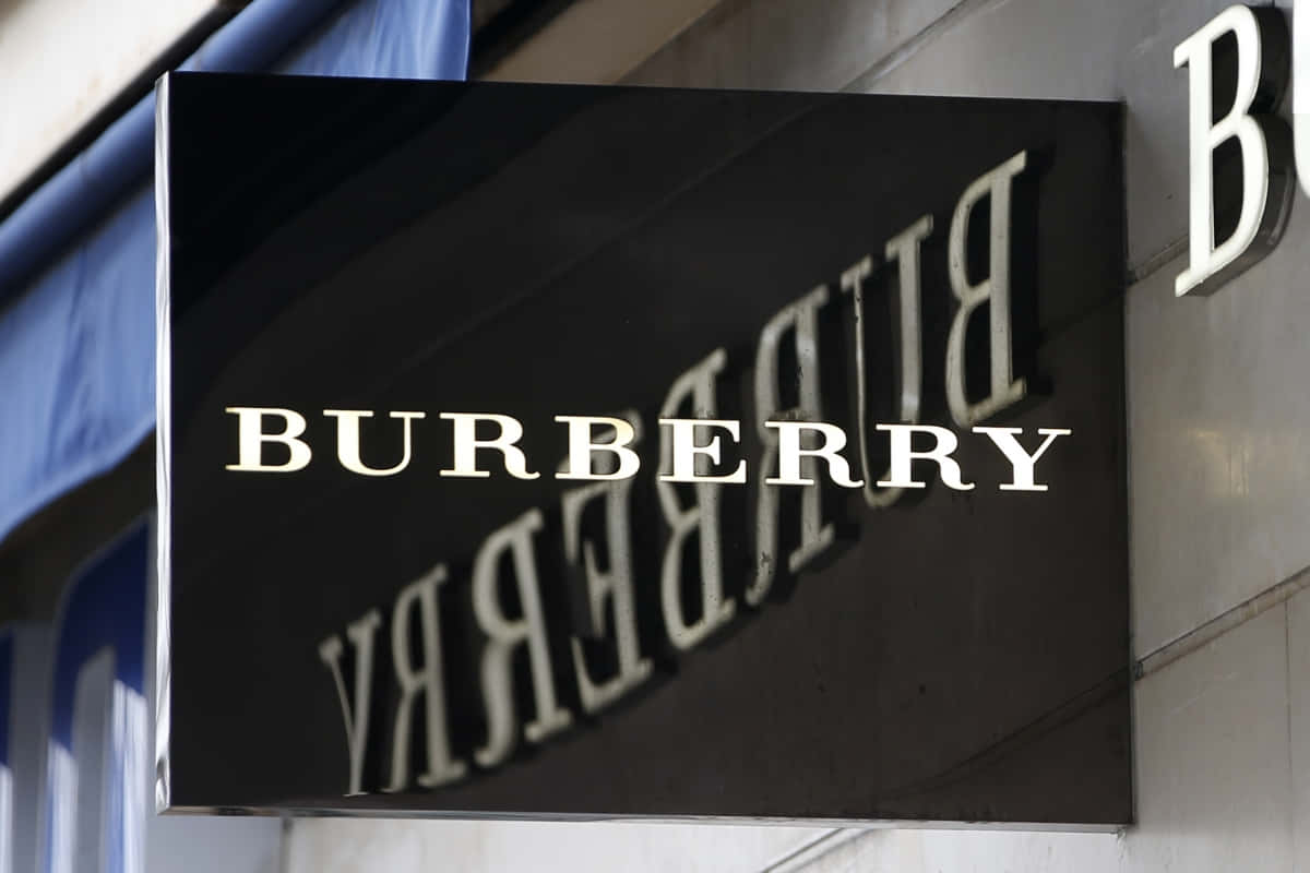 Burberry 的經典風格在 21 世紀重新詮釋 壁紙 — 一個時尚的黑色 Burberry 標誌，帶有白色字體，安裝在建築物外牆上，在日光下。
