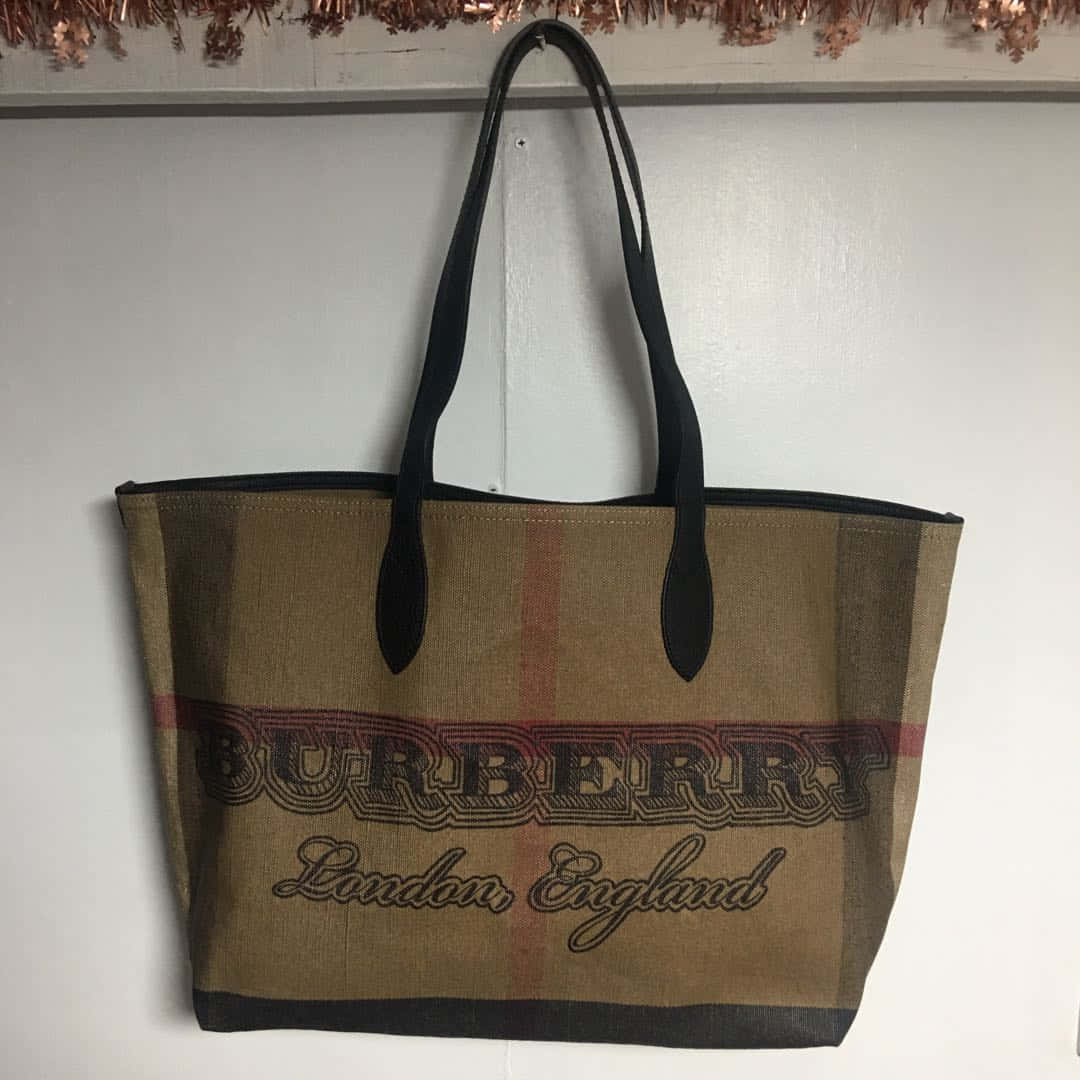 優雅定義：模特攜Burberry手袋 壁紙 — 一個經典格紋的Burberry托特包掛在純白牆上，下方有銅色閃片裝飾。
