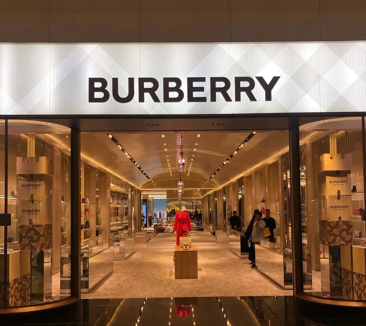 以 Burberry 激發你的時尚靈魂 壁紙 — 豪華的 Burberry 商店入口，配有玻璃門、溫暖的燈光，中央有一個紅色人體模型。