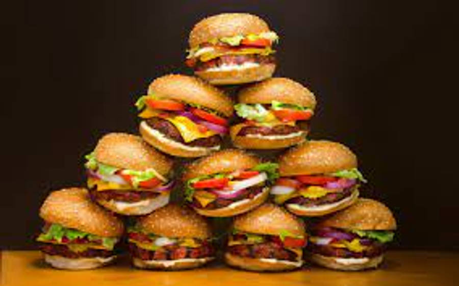 品味皇家風味，盡在 Burger King 壁紙 — 一座高聳的芝士漢堡金字塔，堆疊在木質表面上，背景為深色。