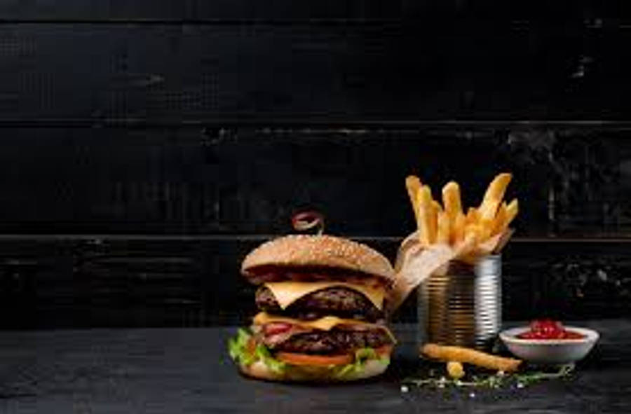 豐盛的 Burger King 用餐組合 壁紙 — 一個多汁的雙層漢堡，配上融化的芝士和新鮮生菜，旁邊是放在深色木桌上罐子裡的金黃酥脆薯條。