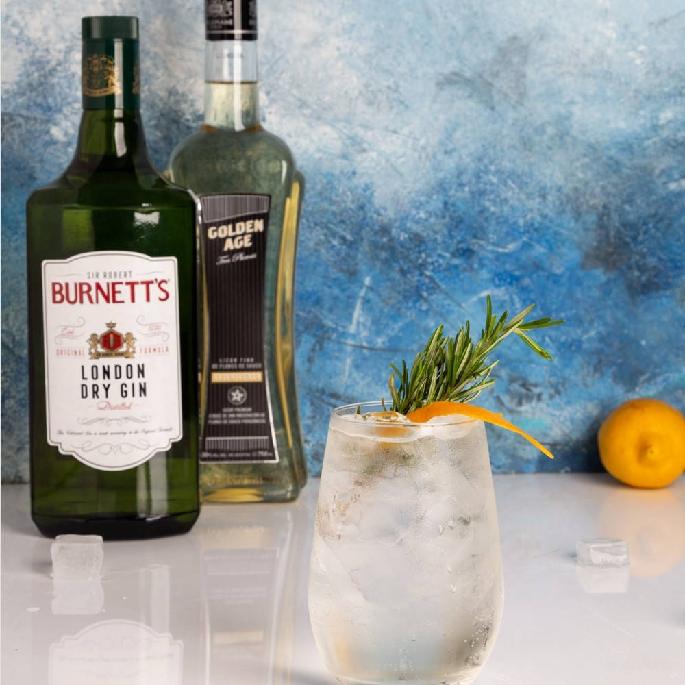 Burnett's 倫敦乾型琴酒搭配 Golden Age 威士忌 壁紙 — 一杯清爽的氈酒雞尾酒，飾以迷迭香和橙皮，放在兩瓶氈酒旁邊，背景是帶紋理的藍色牆壁。