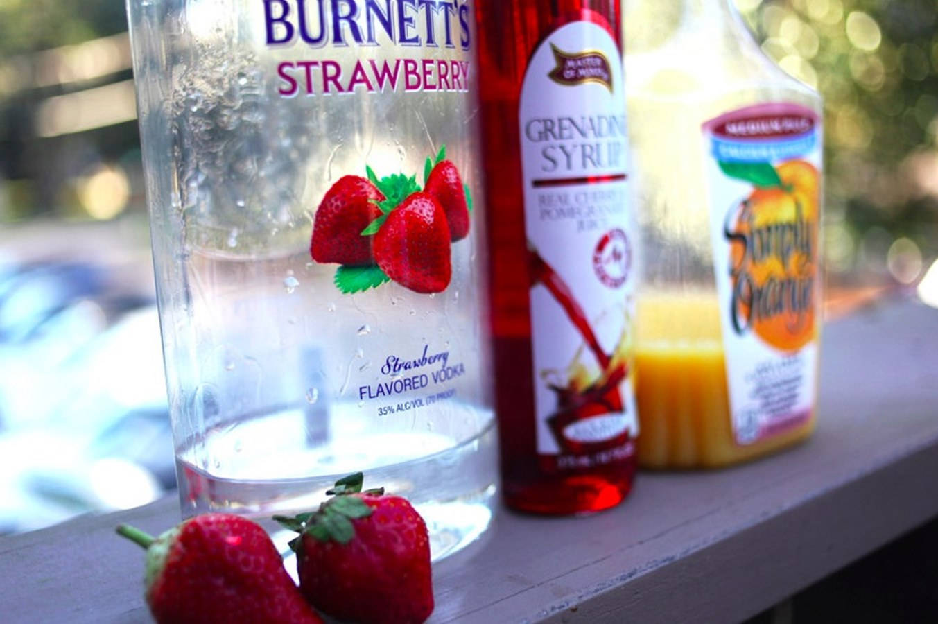 Burnett's 草莓伏特加雞尾酒 壁紙 — 木質表面上嘅士多啤梨伏特加、石榴糖漿同橙糖漿樽嘅特寫，伴隨新鮮士多啤梨。