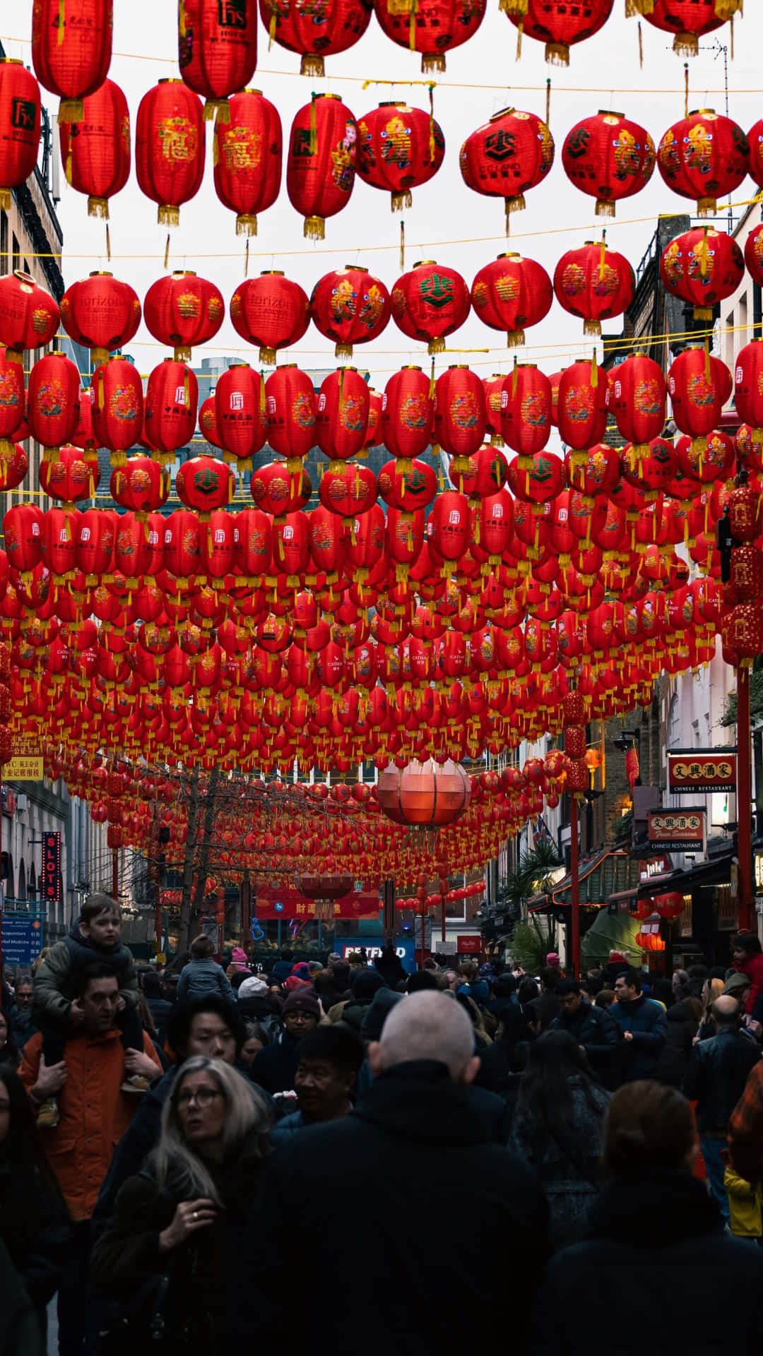  壁紙 — 一條繁忙的街道擠滿了人，頭頂上掛滿了發光的紅色中國燈籠。