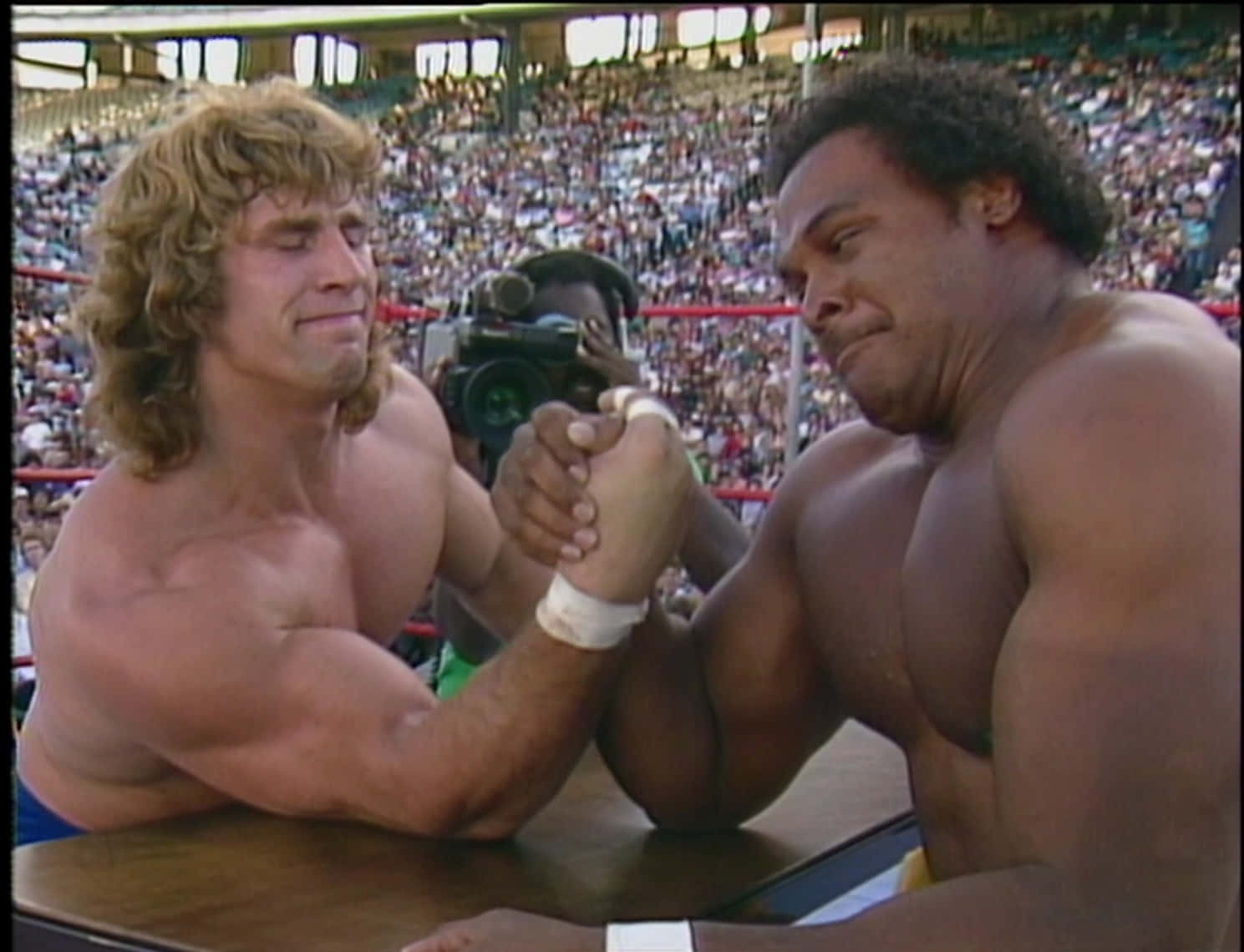 Butch Reed 與 Kerry Von Erich 臂力對決 壁紙 — 兩名肌肉發達的摔角手在擠滿觀眾的競技場中進行激烈的腕力比賽。