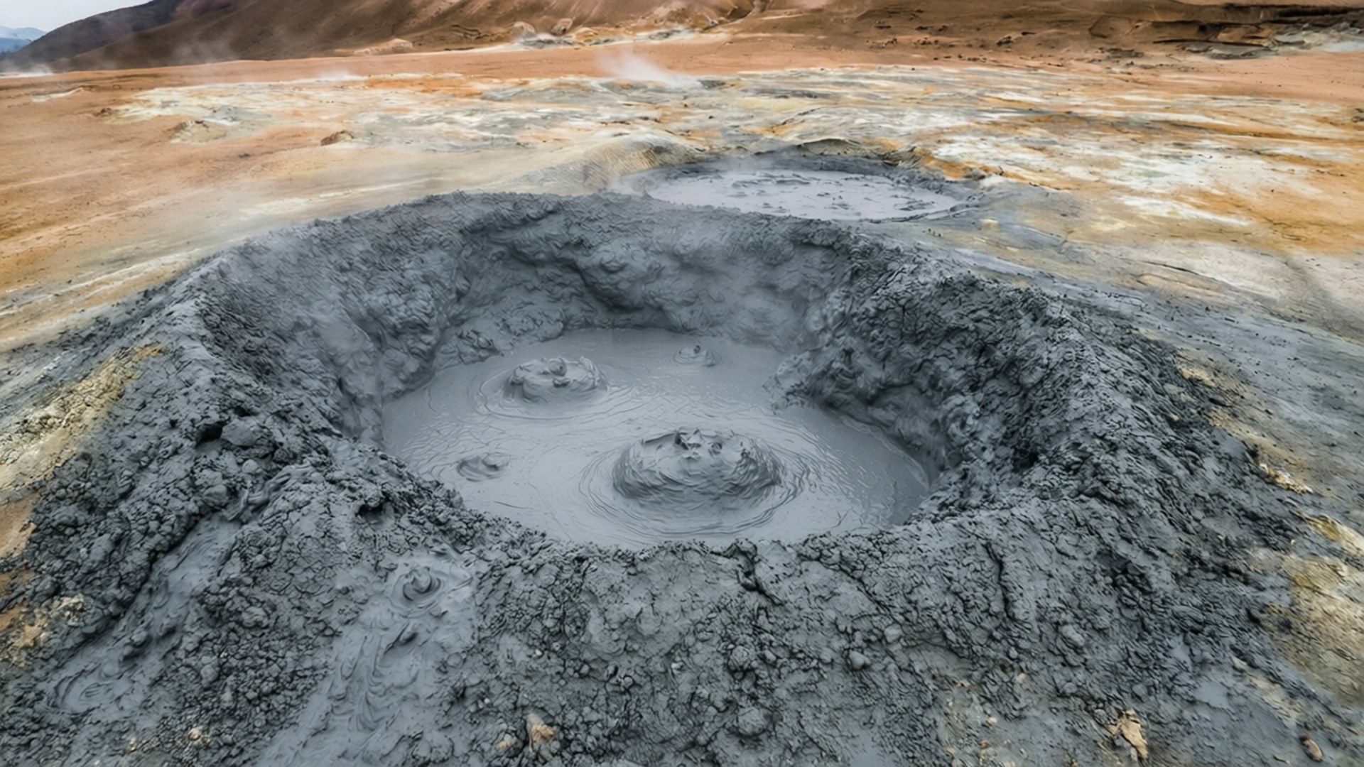 一個冒泡的灰色泥鍋在貧瘠的火山景觀中釋放蒸汽