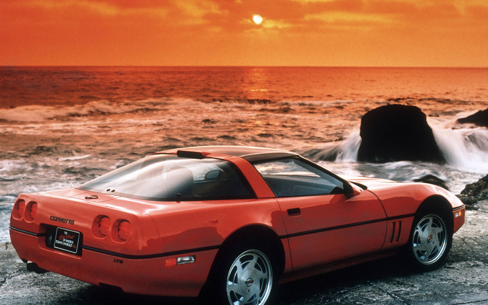 橙色Corvette停泊在岩石海灘，背後有海浪和日落。