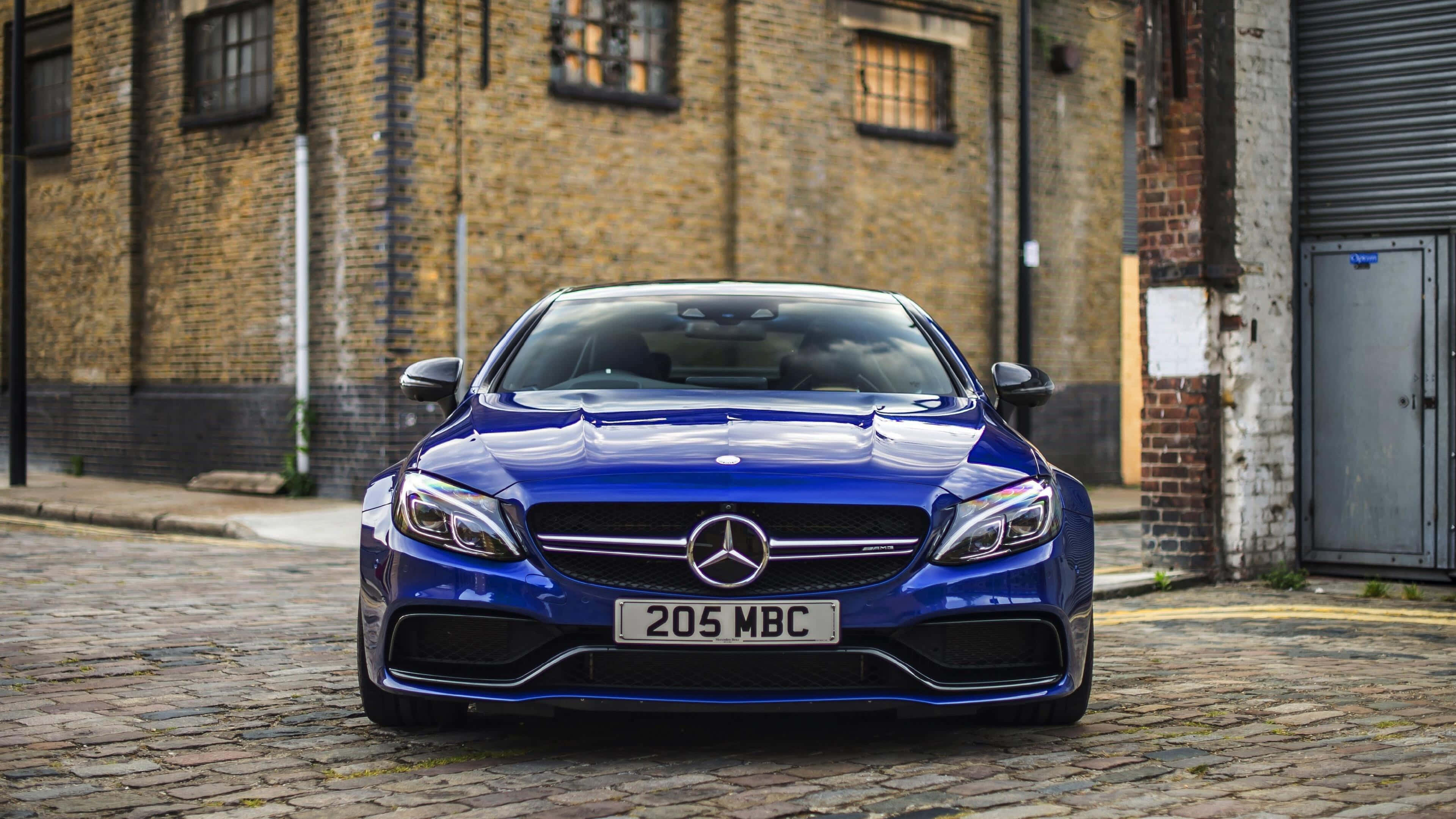 藍色C63 AMG梅賽德斯-奔馳4K 壁紙 — 一架亮藍色嘅Mercedes-AMG C63泊喺鵝卵石街上面，前面係一棟風化咗嘅磚樓。