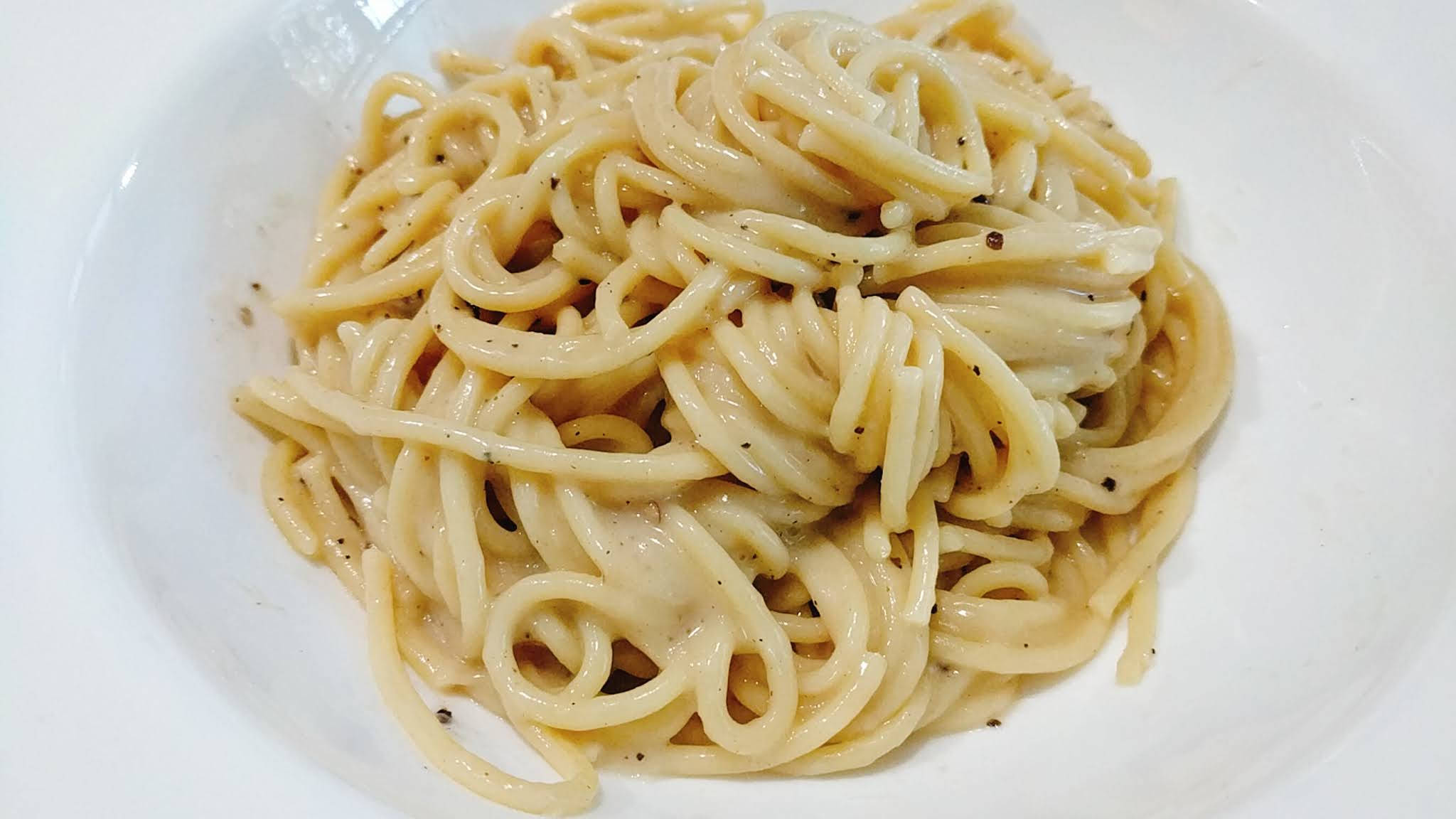 平凡外觀的 Cacio E Pepe 壁紙 — 一個特寫鏡頭，展示放在白色碗中的奶油意粉，上面撒有黑胡椒。