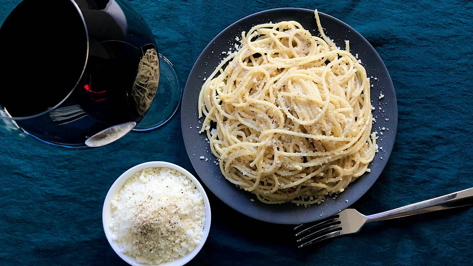 搭配紅酒的 Cacio E Pepe 壁紙 — 一碟忌廉意粉配磨碎芝士，旁邊放著一杯紅酒，置於深藍色紋理枱布上。