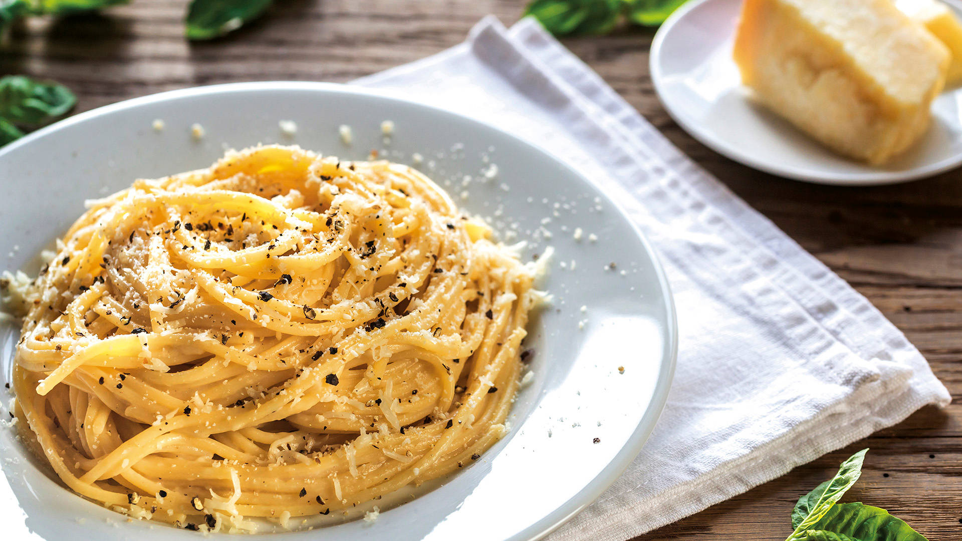 Cacio E Pepe 晚餐 壁紙 — 一盤奶油意粉配磨碎芝士和黑胡椒，放在木桌上，旁邊有巴馬臣芝士和新鮮羅勒。