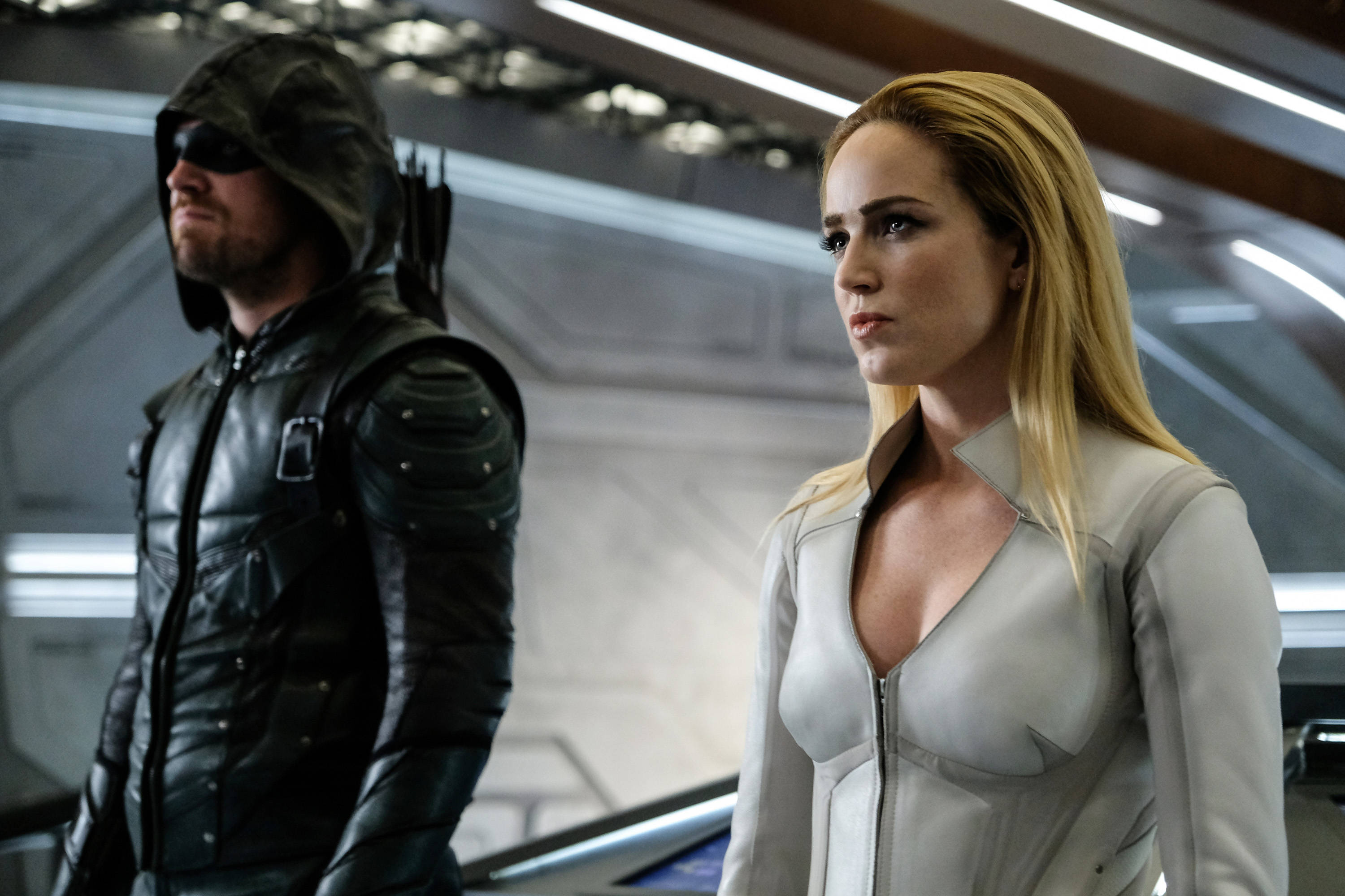 Caity Lotz 與 Oliver Queen 壁紙 — 兩位超級英雄站在未來風格的太空船走廊上，一位身穿黑色連帽盔甲，另一位身穿白色緊身衣。