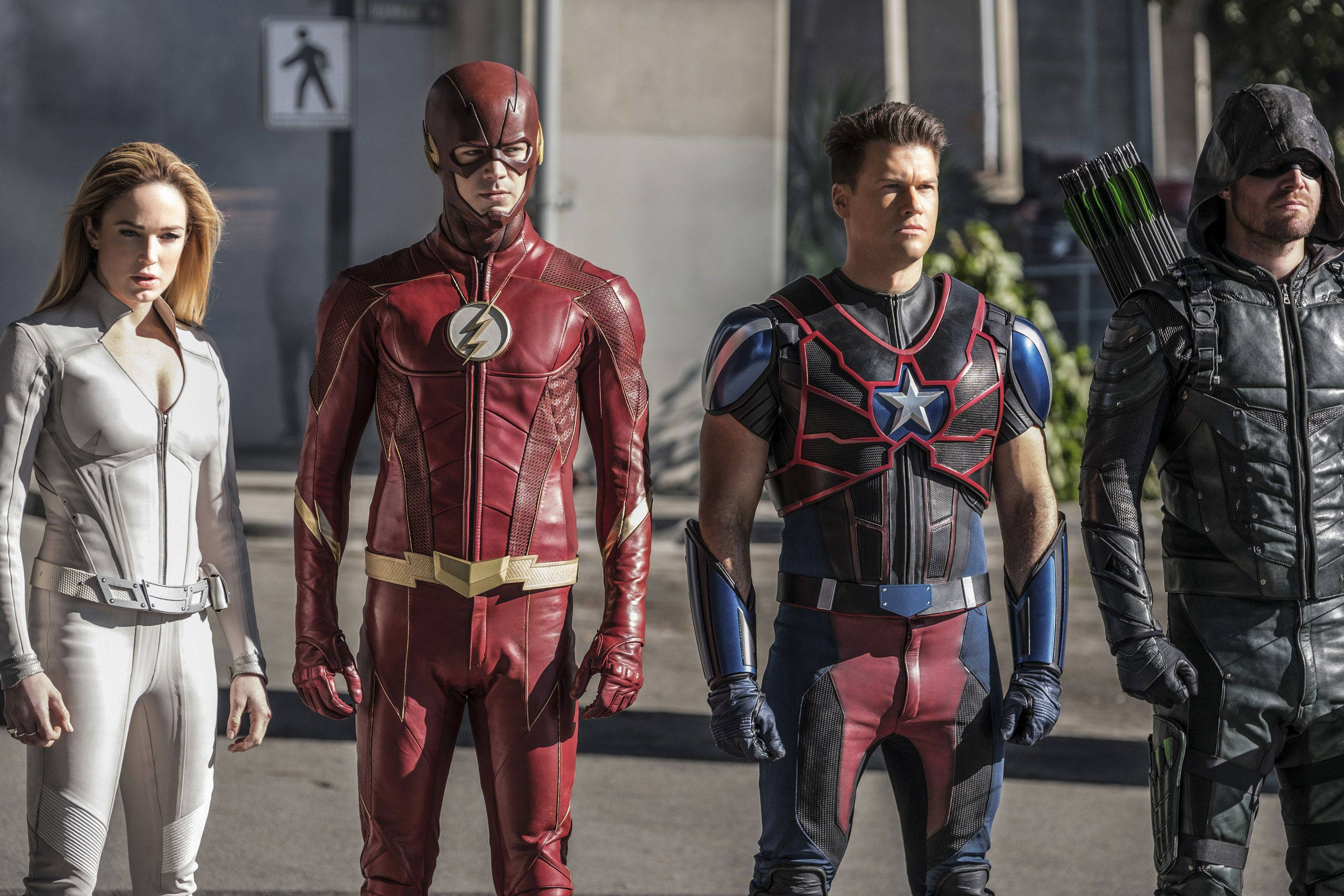 Caity Lotz 在 DC 交叉劇集拍攝現場 壁紙 — 四位超級英雄穿著精細服裝，在明亮的日光下，站在城市行人道上一字排開。