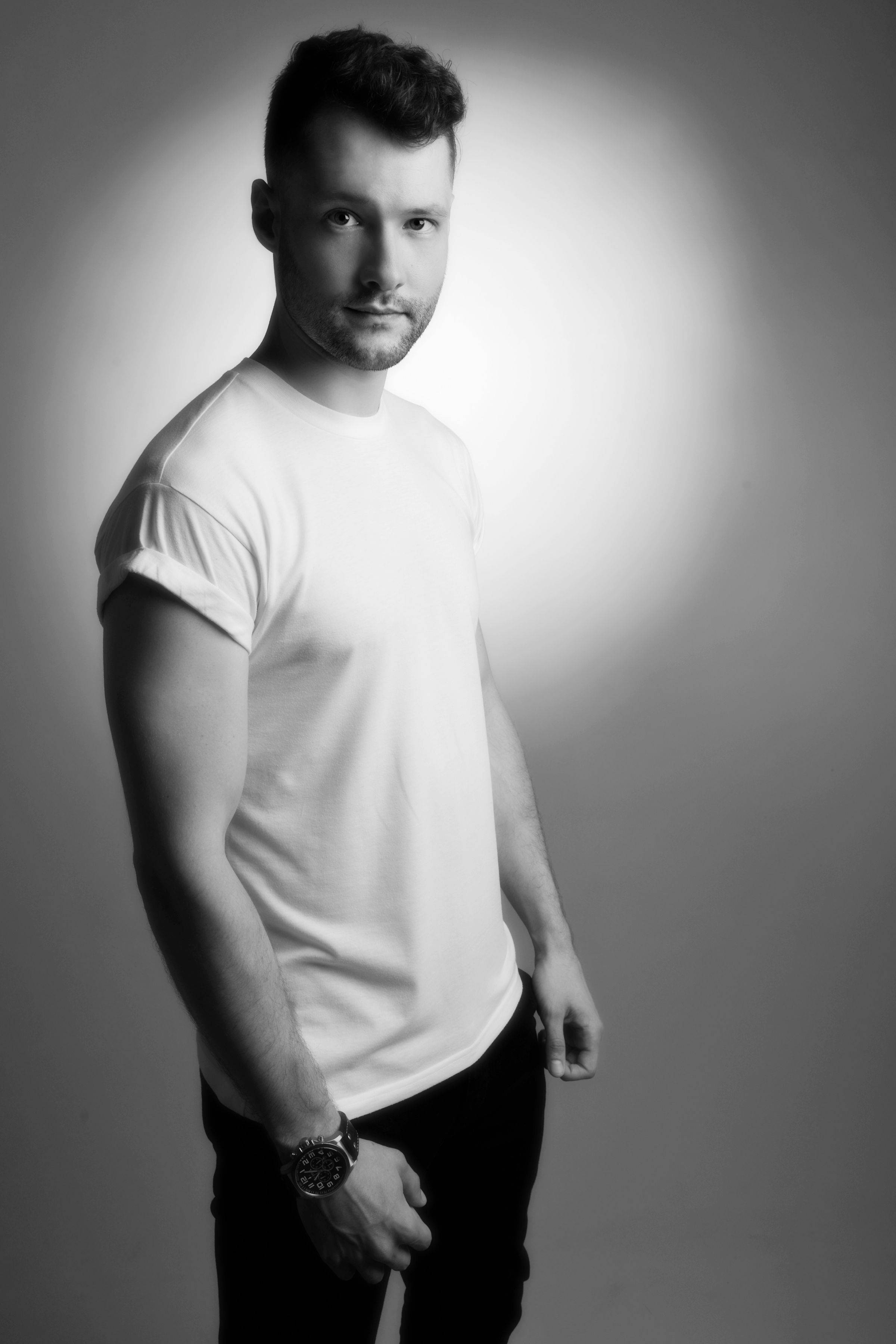 Calum Scott 單色寫真 壁紙 — 一個自信嘅男人著住白色T恤，企喺柔和燈光嘅灰色背景前，配合戲劇性嘅攝影棚燈光。