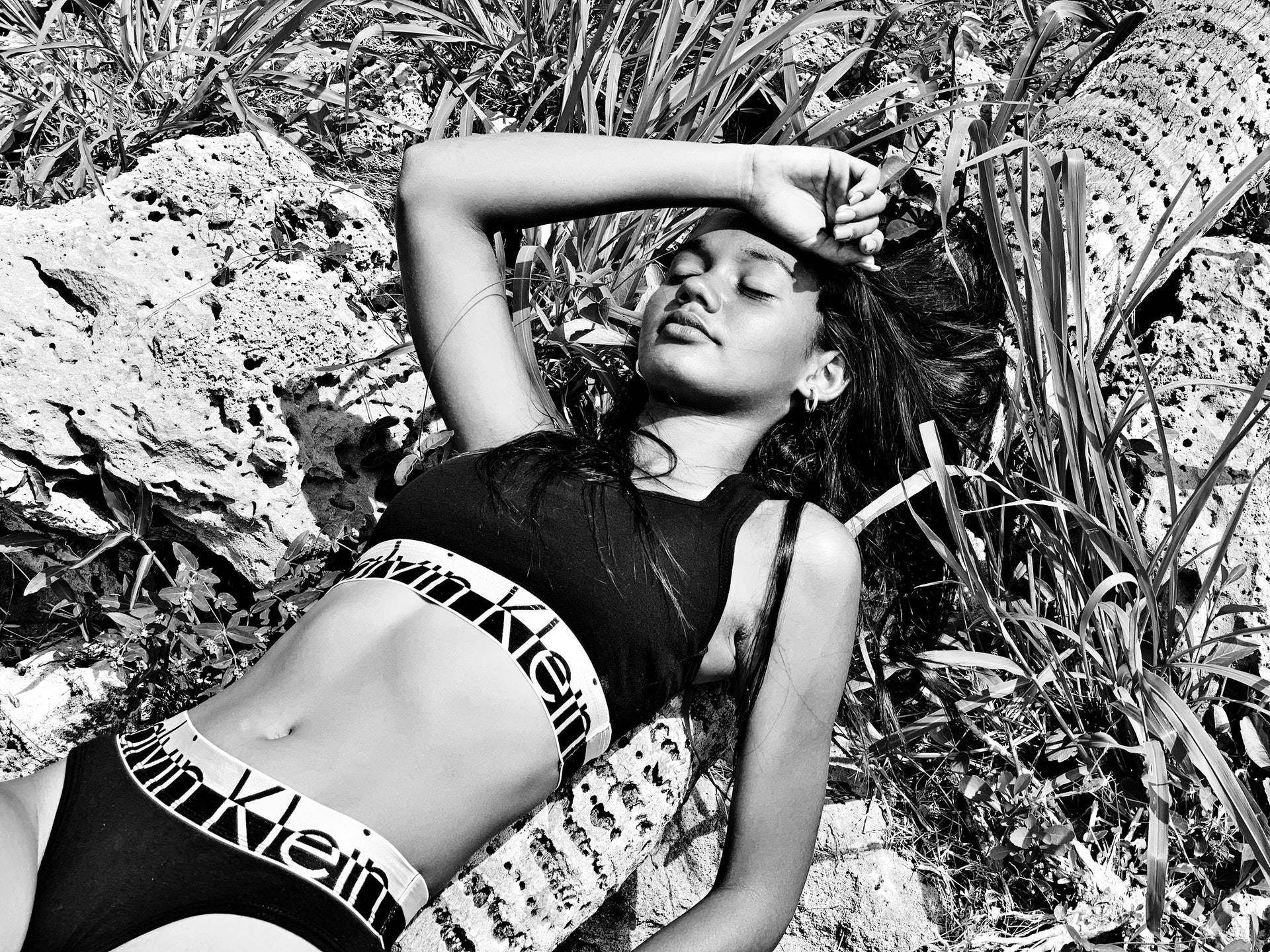 穿著Calvin Klein泳衣的女性在黑白植物間的岩石上放鬆。