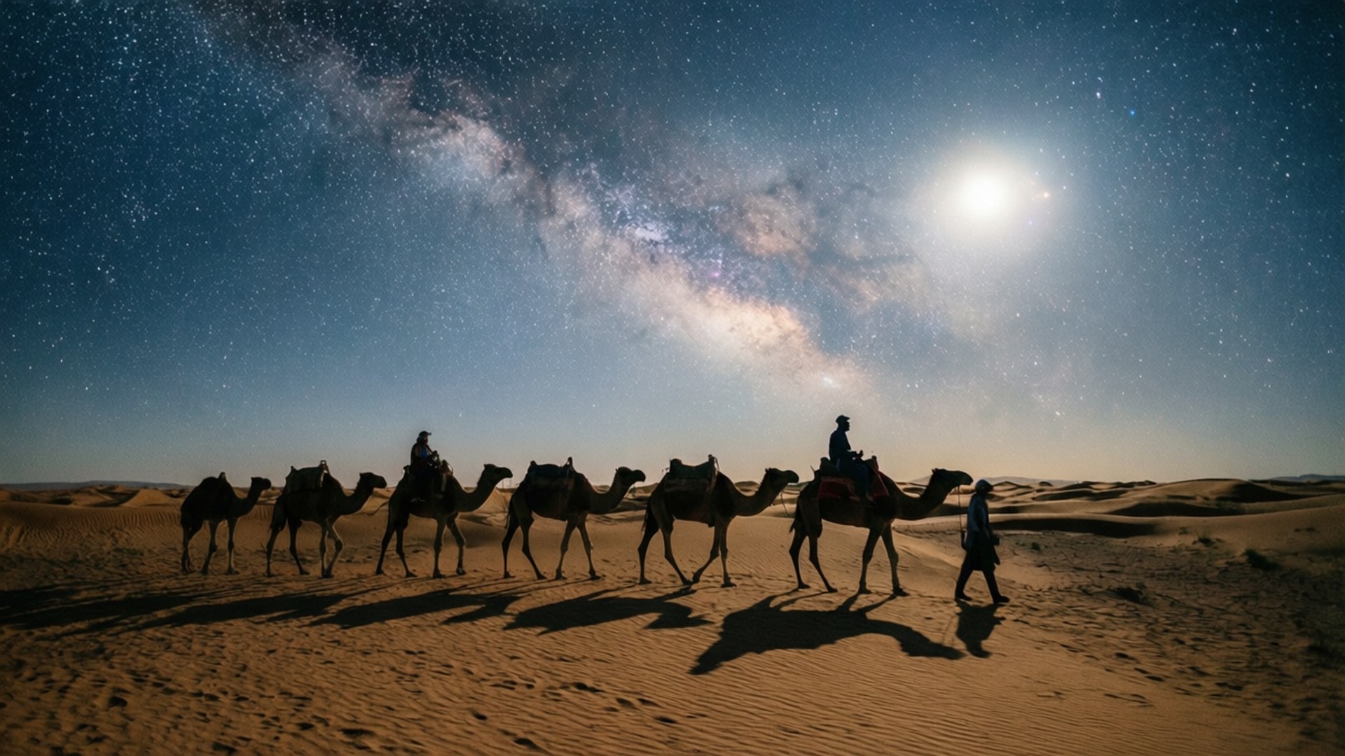 駱駝和騎手在星空夜空下穿越沙漠沙丘，伴隨著明亮的月亮。