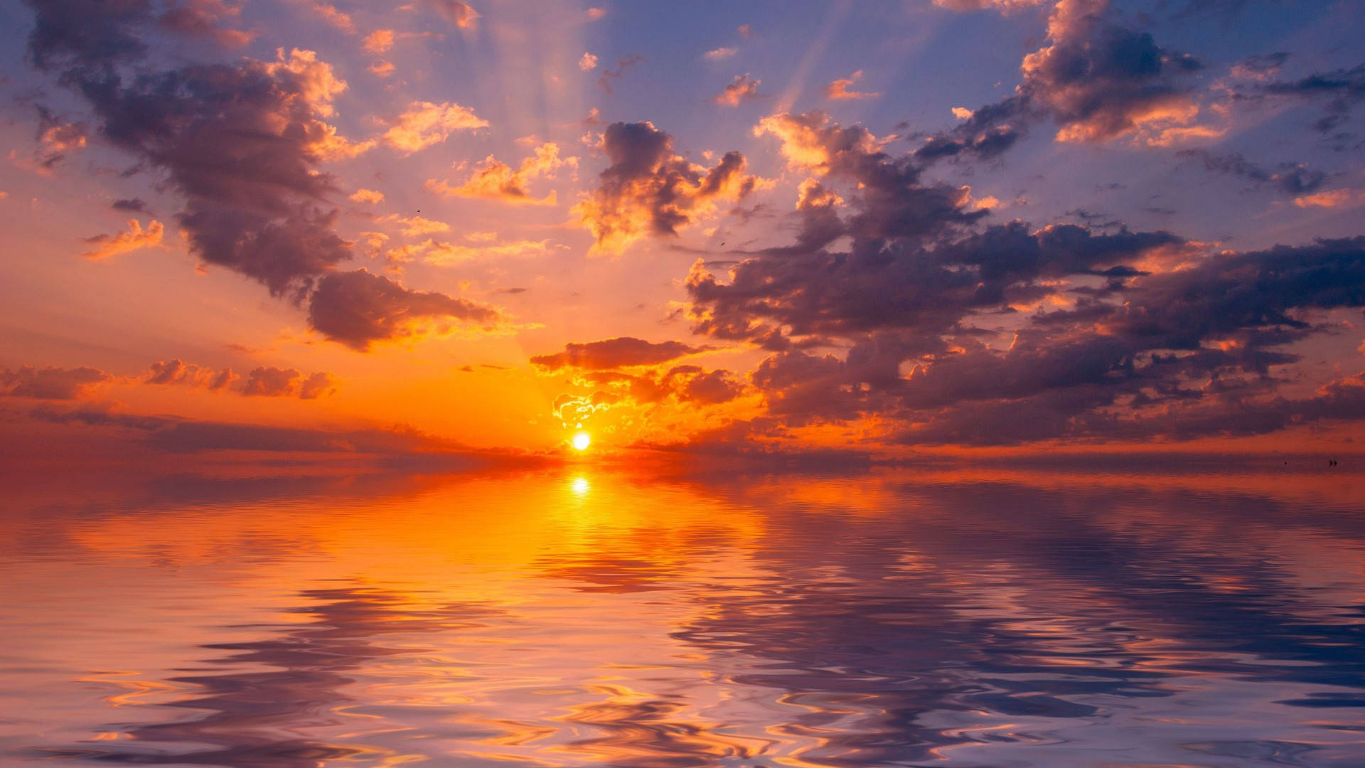 迷人的地平線天空 壁紙 — 燦爛的夕陽在平靜的海洋上投射出火熱的橙色和紫色色調，陽光穿過戲劇性的雲層。