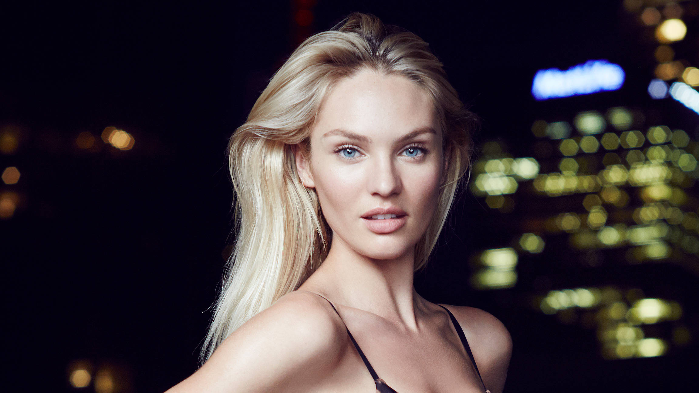 Candice Swanepoel 城市夜景攝影 壁紙 — 一位金髮碧眼的女性在模糊的夜間城市燈光背景下凝視前方。
