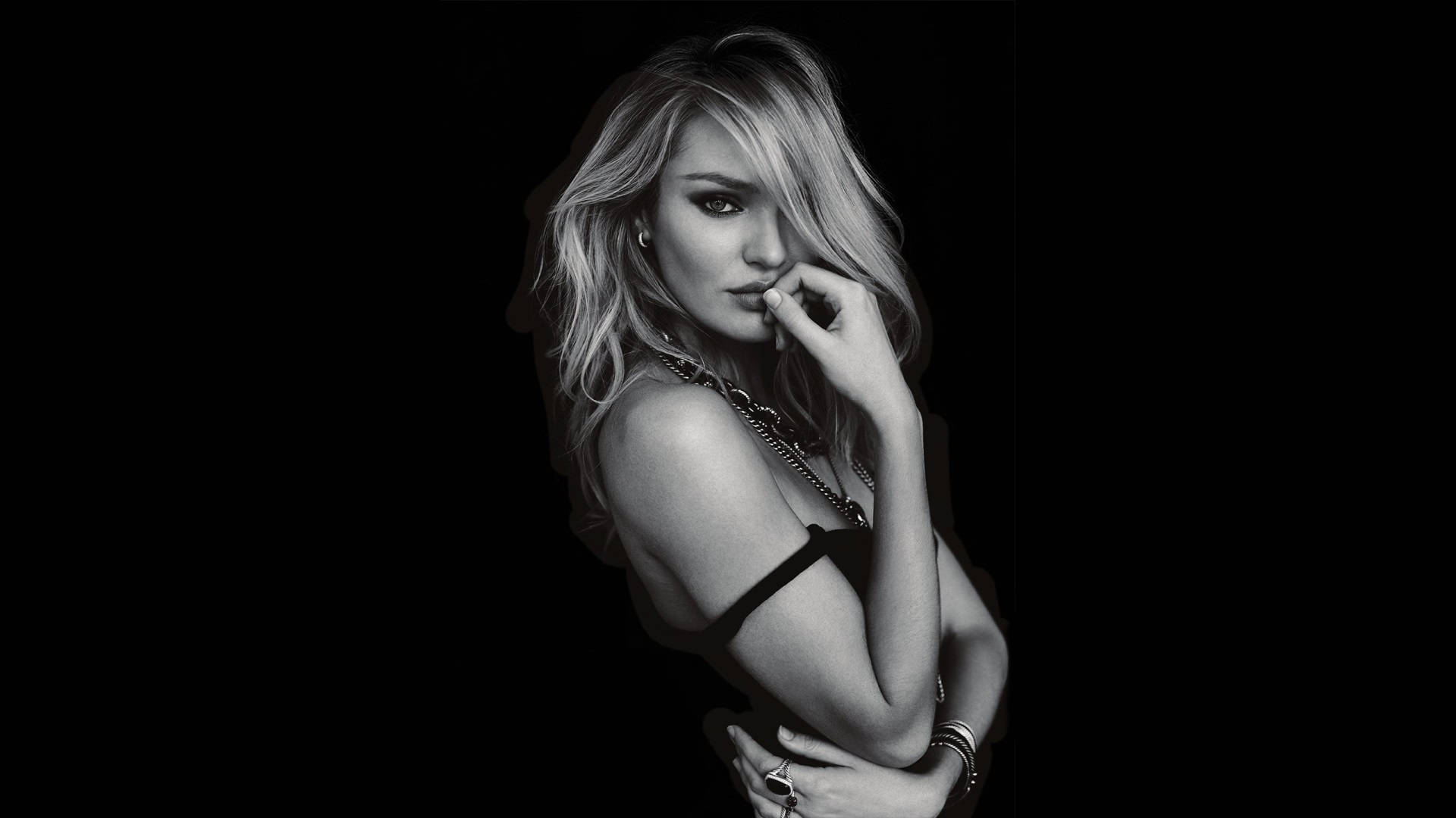 Candice Swanepoel 單色攝影 壁紙 — 一個引人注目的黑白肖像，一位金髮女性在深色背景前將手靠近嘴唇。