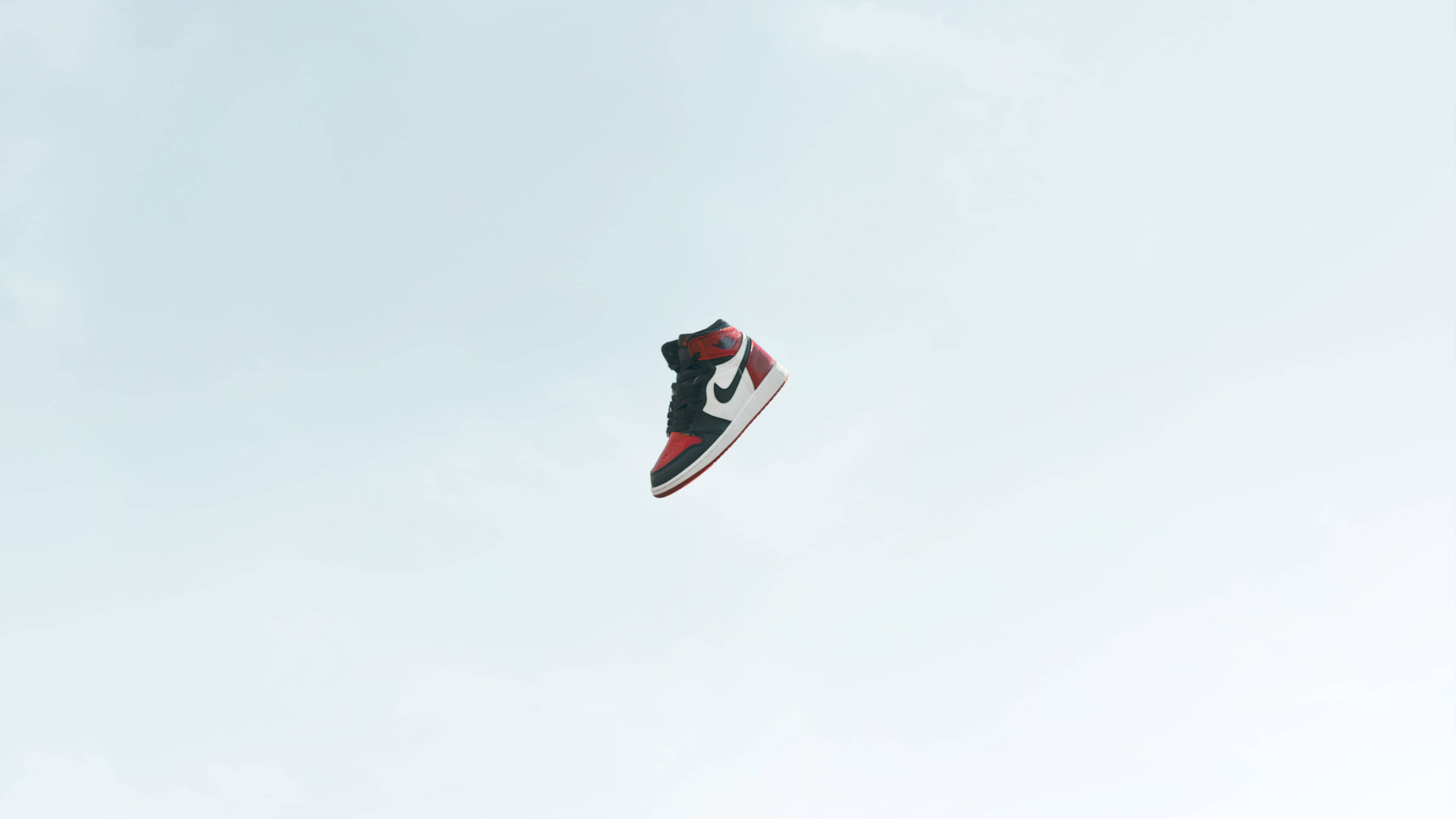 Canva Air Jordan數位攝影 壁紙 — 一隻黑色、紅色和白色的運動鞋獨自漂浮在蒼白的多雲天空中。