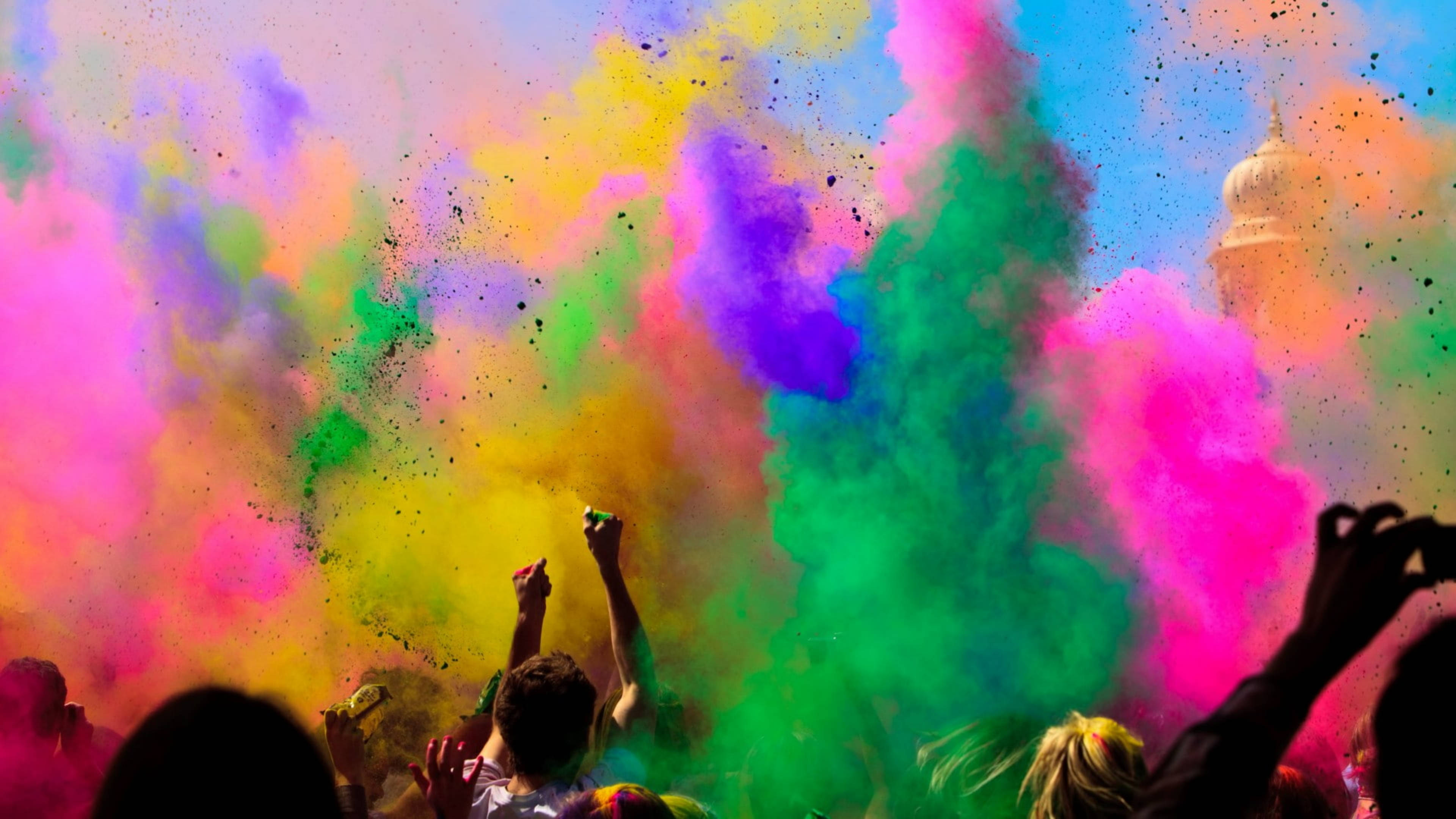 Canva 彩煙爆破 壁紙 — 鮮豔的粉末像萬花筒般爆發，人們在明亮的天空下舉手慶祝。