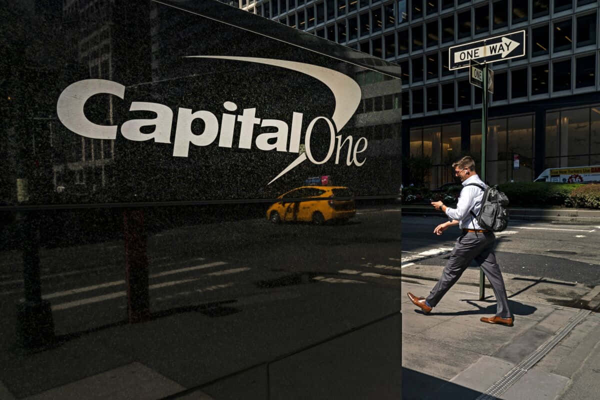 Capital One 標誌於大理石牆面 壁紙 — 一名商人走過 Capital One 大樓，一輛黃色的士在明亮的日光下反射在其玻璃外牆上。