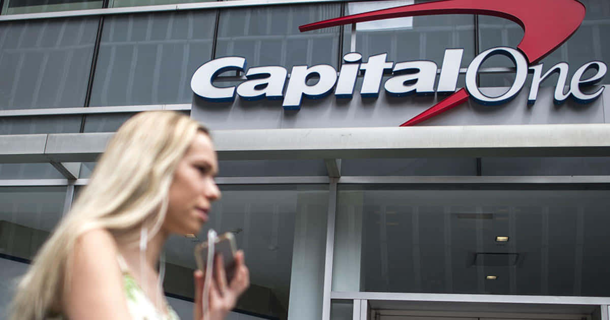 金髮女子走過 Capital One 銀行，同時使用手機。