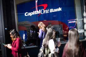 人們在夜晚走過一間Capital One Bank，帶有發光的標牌。