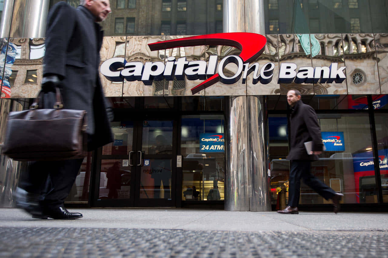 兩名商人走過一間設有玻璃門和24小時自動櫃員機標誌的Capital One銀行。