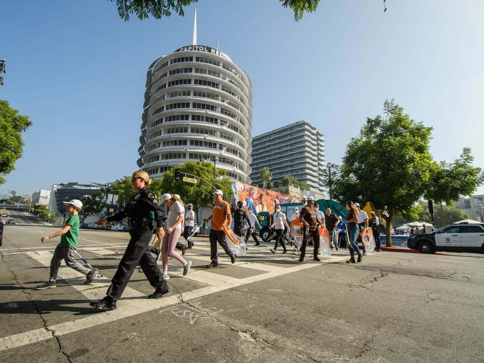 Capitol Records大樓街頭的人群 壁紙 — 一名警察引導行人穿過陽光明媚的街道，前方是標誌性的 Capitol Records 大樓。