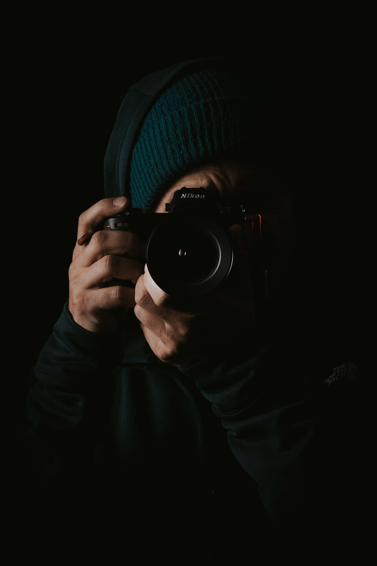 穿著深色連帽衫和冷帽的人在陰影中拿著Nikon相機。