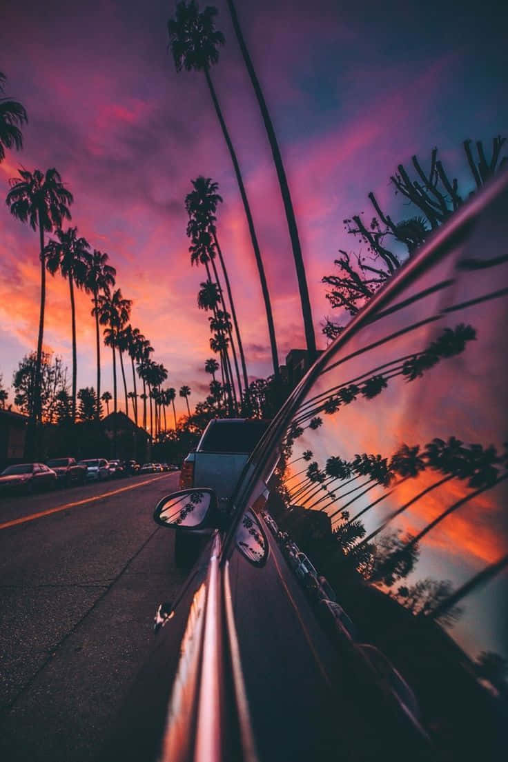 Sunset Drive 桌布 壁紙 — 汽車側鏡反射出充滿活力的日落天空，棕櫚樹在深紫色和橙色色調下排列在道路兩旁。