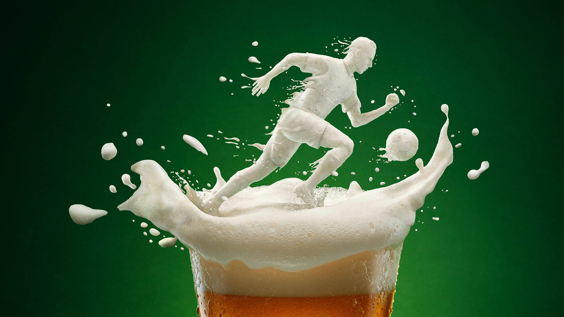 Carlsberg啤酒創意飲品 壁紙 — 一個用啤酒泡沫雕刻而成的足球員和足球，從玻璃杯中動態躍出，背景是深綠色。