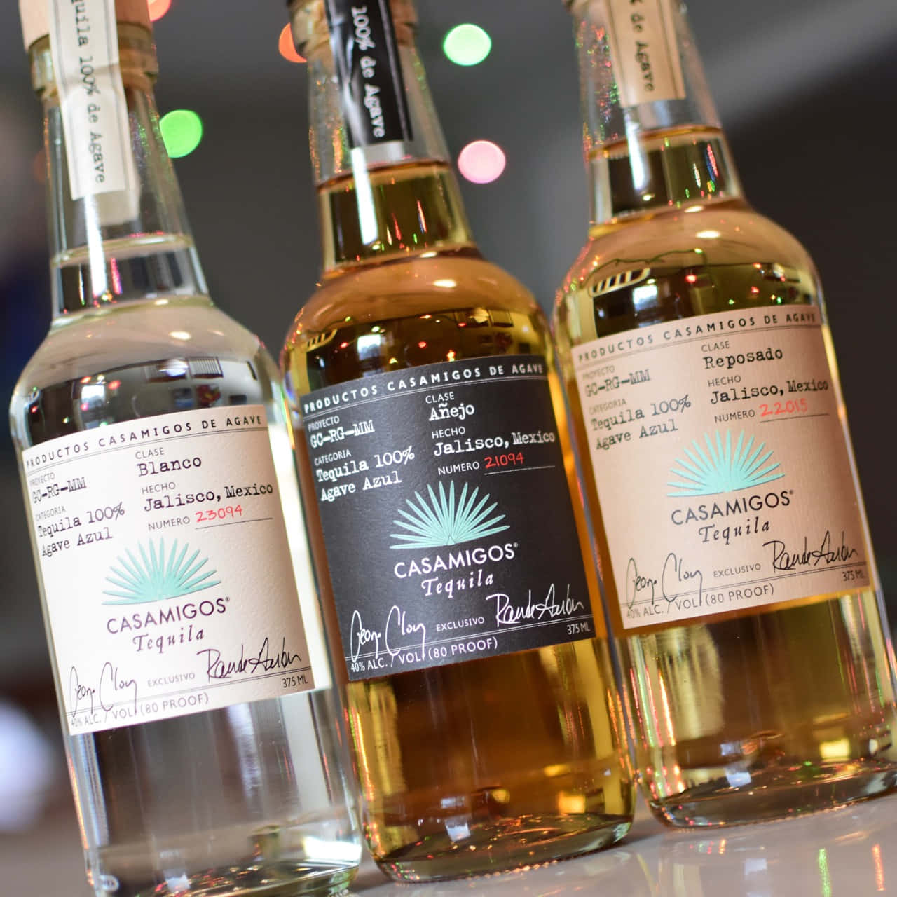 三支 Casamigos 龍舌蘭酒瓶，背景有色彩繽紛的模糊燈光。