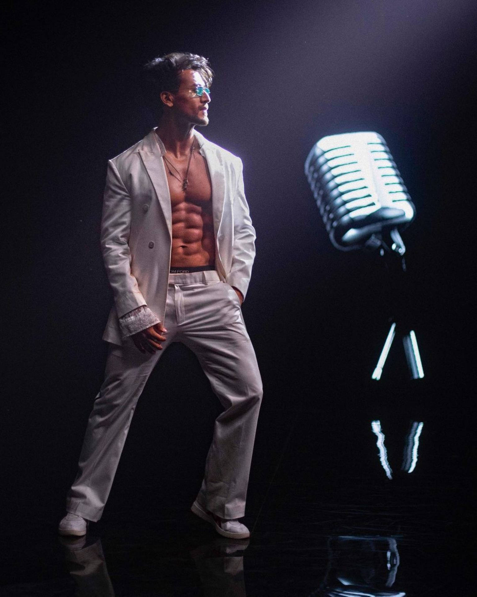 《Casanova》歌曲演唱的提格·沙羅夫 壁紙 — 一個肌肉發達的男人穿著白色西裝，自信地站在黑暗反光舞台上一個發光的復古麥克風旁邊。