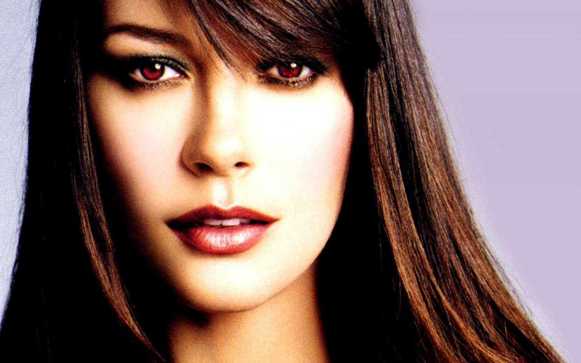 Catherine Zeta-Jones 深棕色長髮 壁紙 — 近距離肖像照，一位擁有引人注目的紅眼睛和深色頭髮的女性，背景是柔和的薰衣草色。