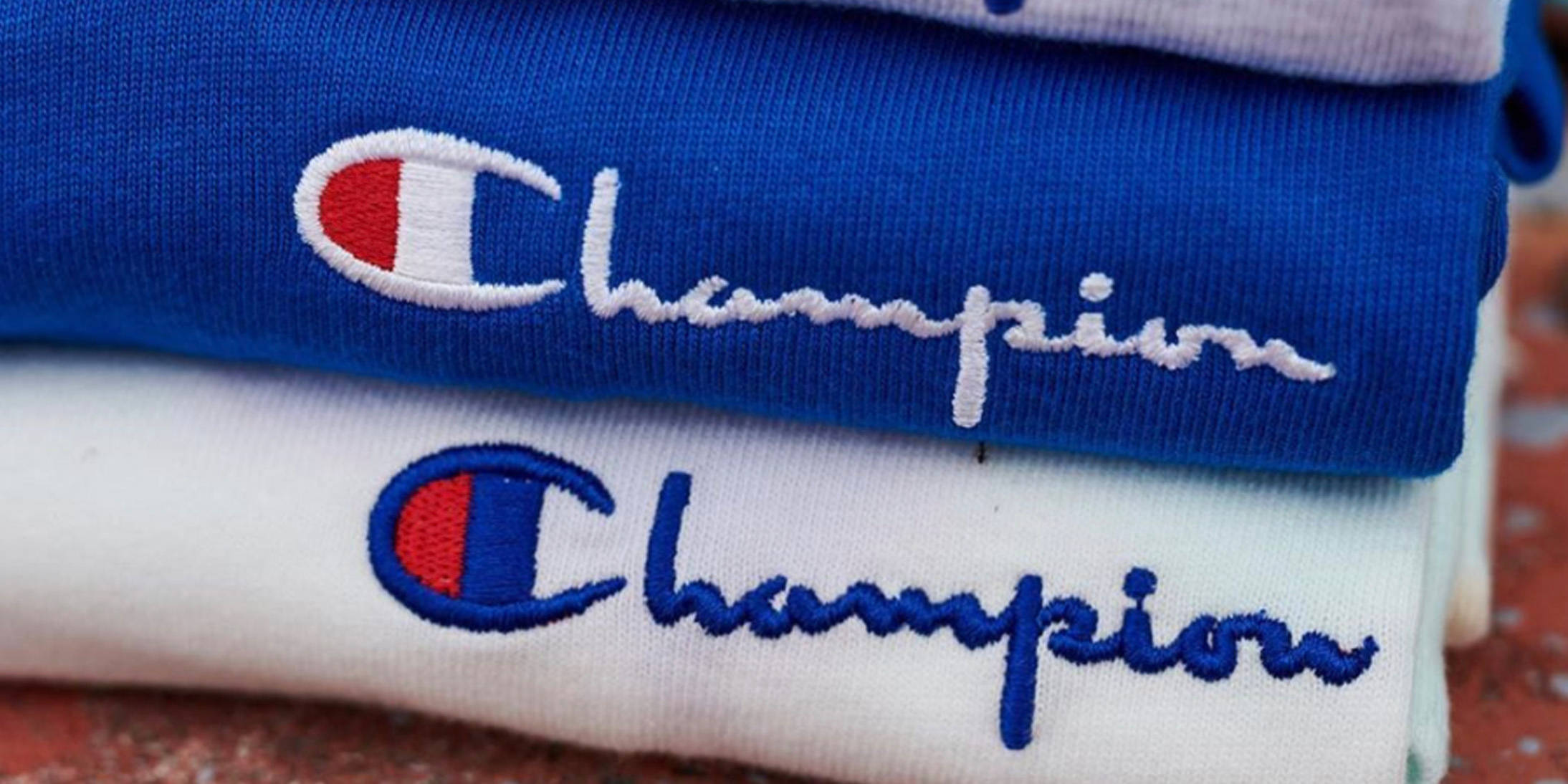 Champion 堆疊服裝 壁紙 — 藍色和白色Champion衛衣堆疊，帶有刺繡標誌的特寫細節。