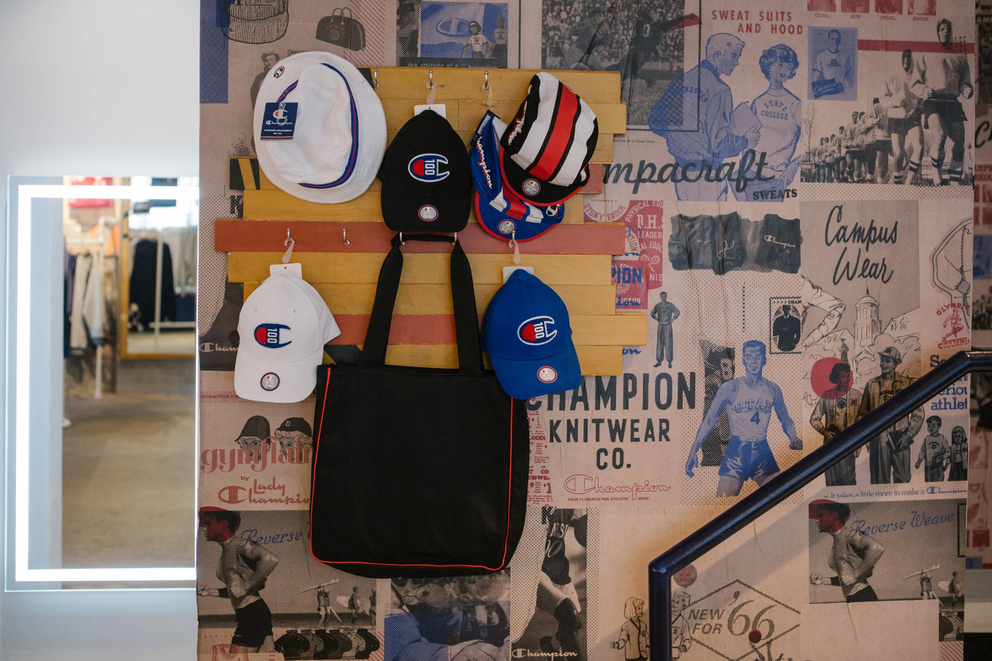 Champion 多款配件 壁紙 — 復古Champion品牌帽子展示，配有復古運動海報和一個黑色手提袋掛在木架上。