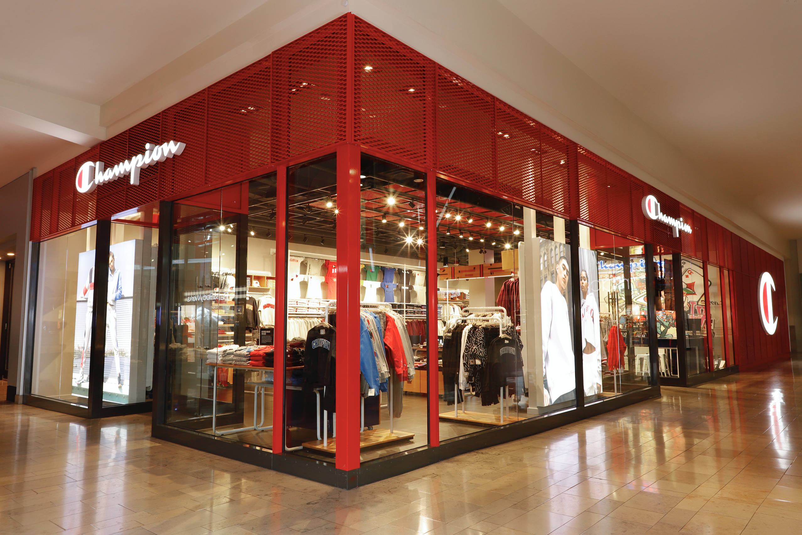 Champion紅色特賣店 壁紙 — 一間光線充足的Champion運動服飾店，配有紅色金屬面板和玻璃窗，在購物中心內展示運動服裝。