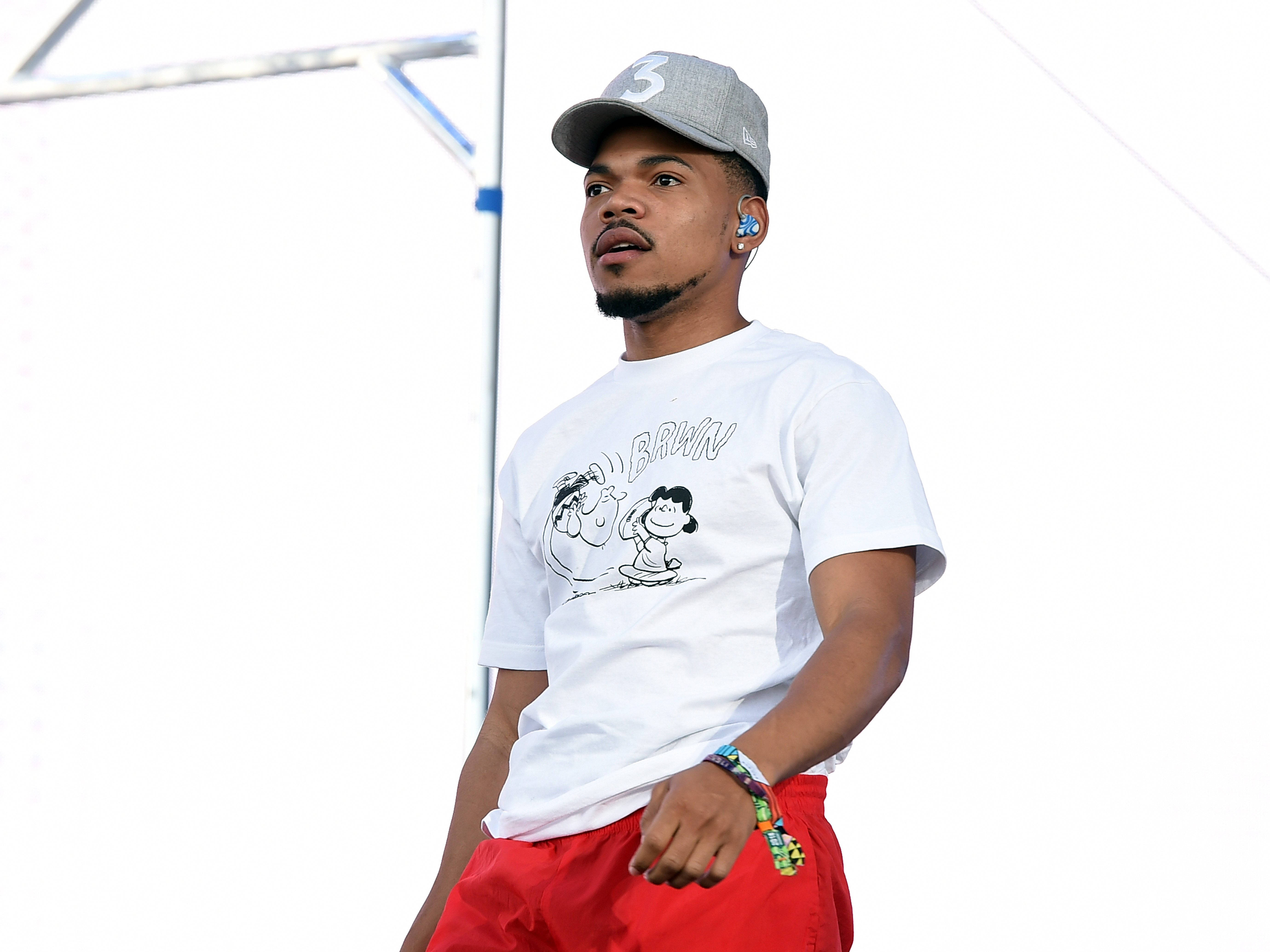 Chance The Rapper 貝納特卡通 壁紙 — 一位戴灰色帽子和紅色短褲的年輕男子自信地站著，身穿帶有卡通圖案的白色T恤。