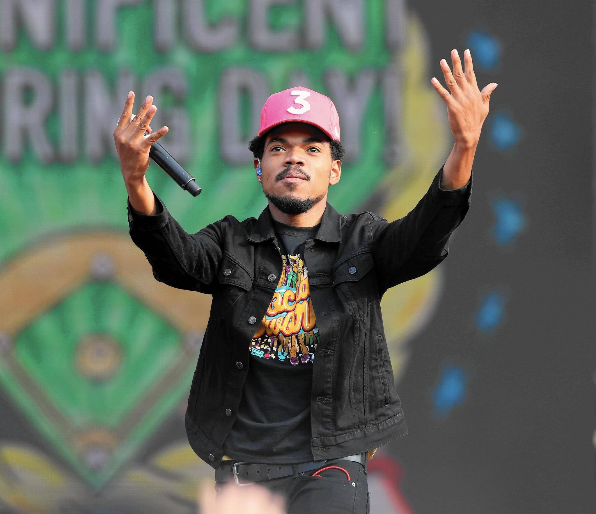 Chance The Rapper 手舉高高 壁紙 — 音樂家戴著粉紅色帽子和黑色外套，雙手舉起拿著麥克風在舞台上表演。