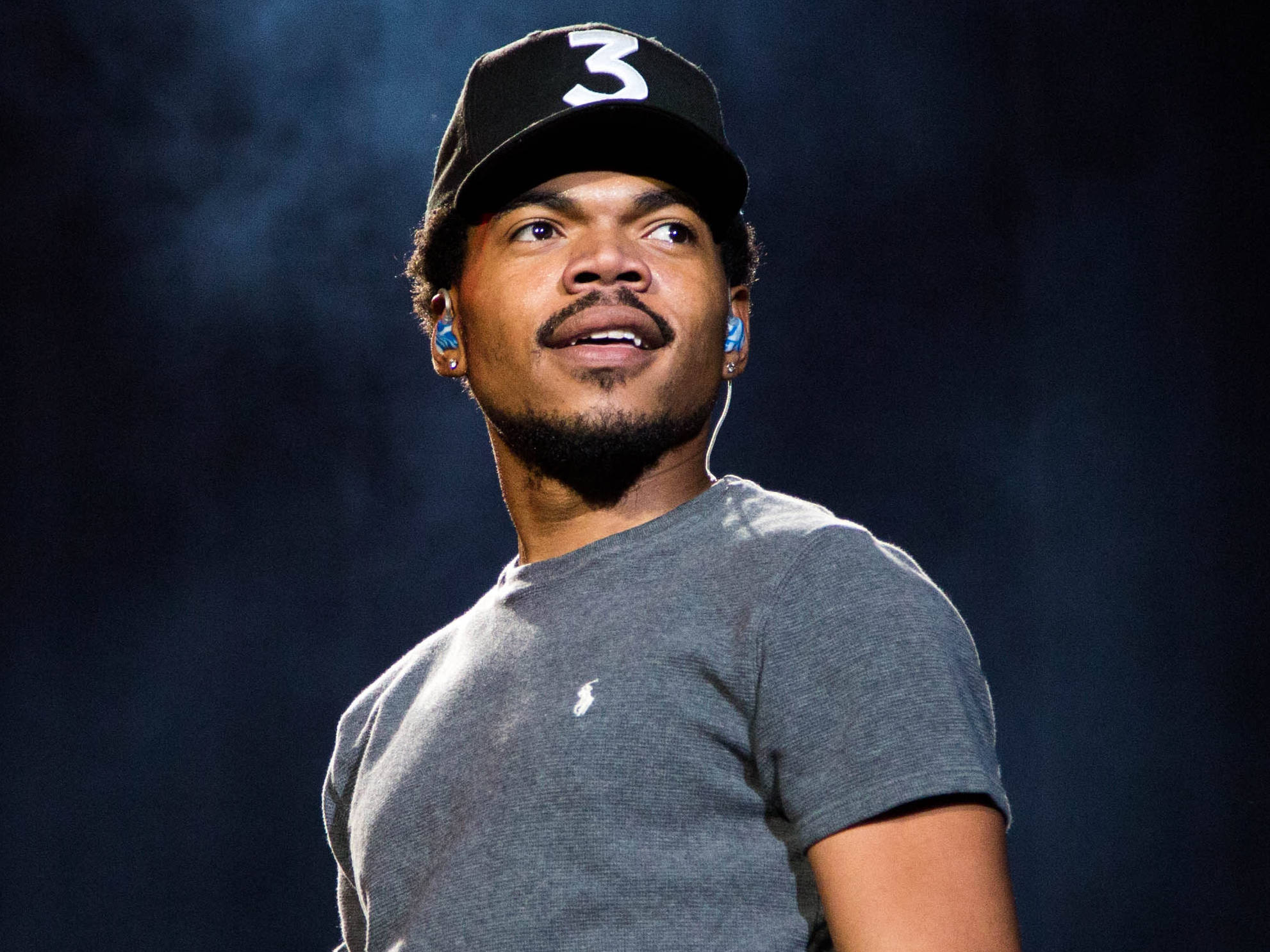 Chance the Rapper煙霧演出 壁紙 — 一名戴著黑色帽子、上面有白色數字三和藍色耳機的男子，在黑暗煙霧背景中表情豐富地向上望。