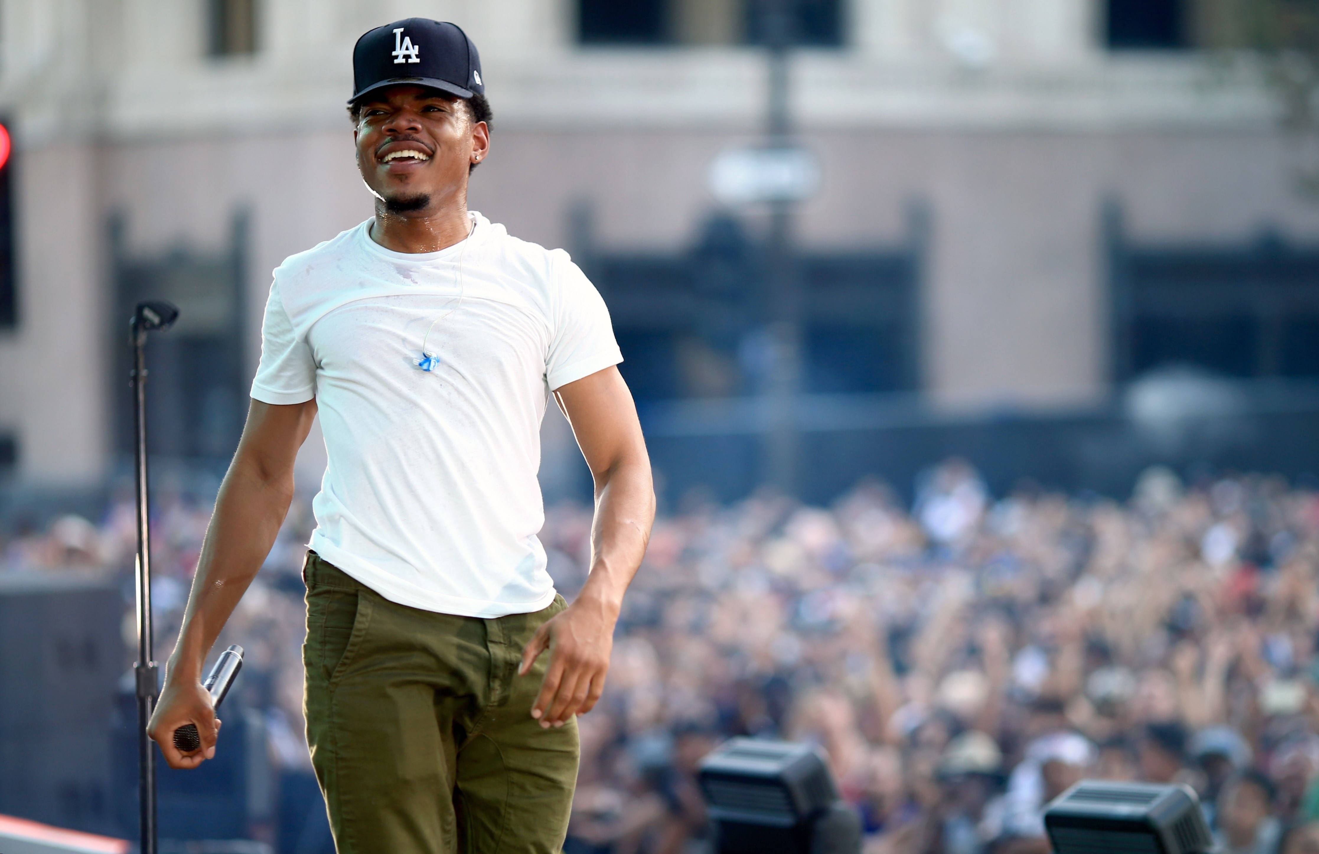 Chance The Rapper 群眾前演出 壁紙 — 一位身穿白色T恤和帽子的微笑表演者自信地走在舞台上，面對歡呼的人群。