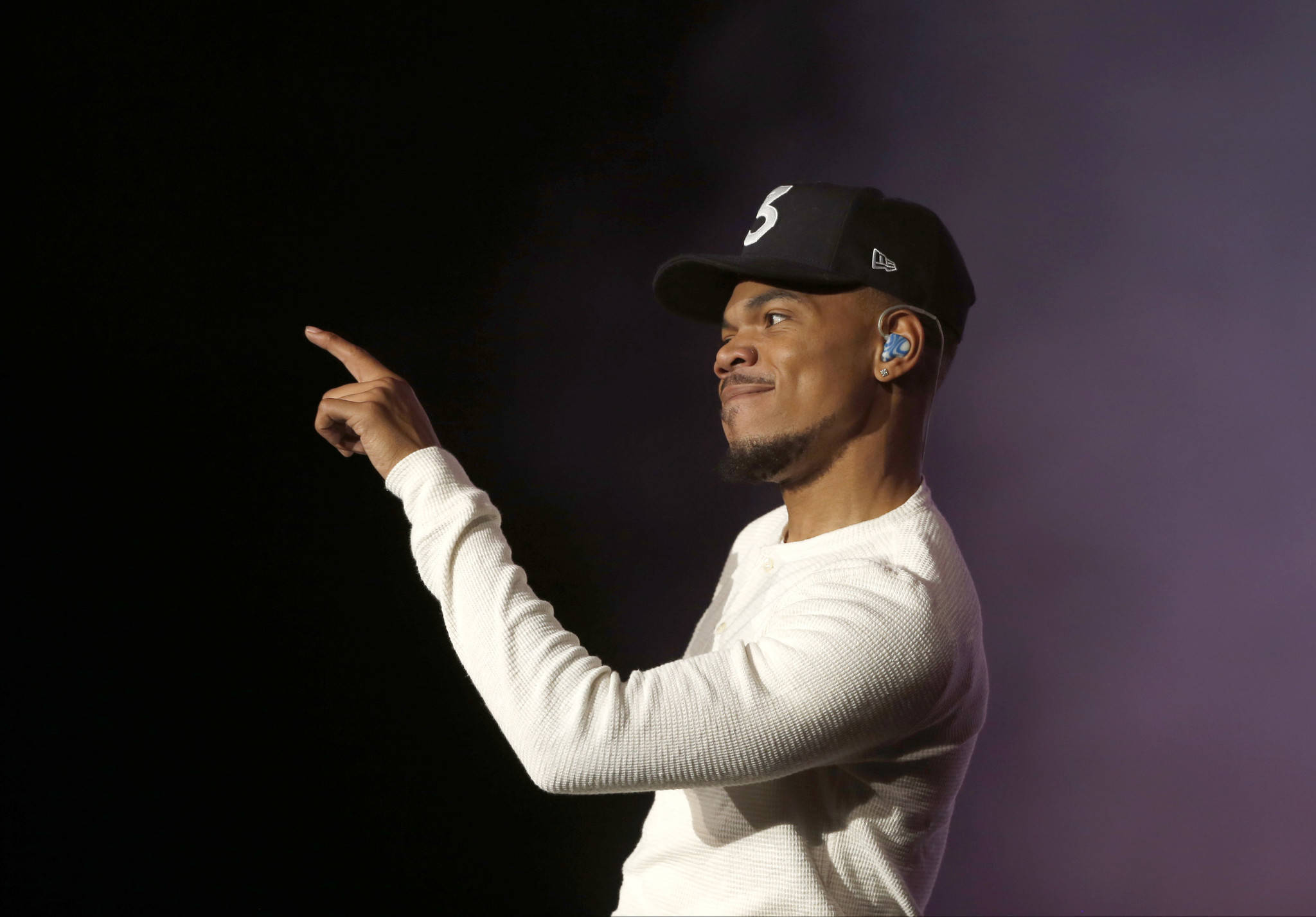 Chance The Rapper 演唱會歡樂時刻 壁紙 — 一名身穿白色長袖襯衫和黑色帽子的男子，在深紫色燈光背景下自信地指著。