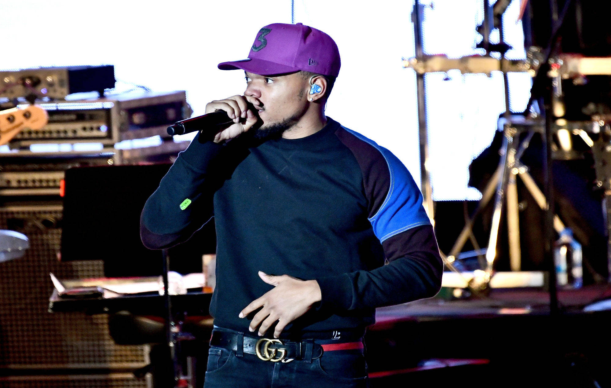 Chance The Rapper 紫色帽子 壁紙 — 一位戴著紫色帽子和黑色襯衫的男性饒舌歌手在燈光明亮的舞台上對著麥克風熱情表演。